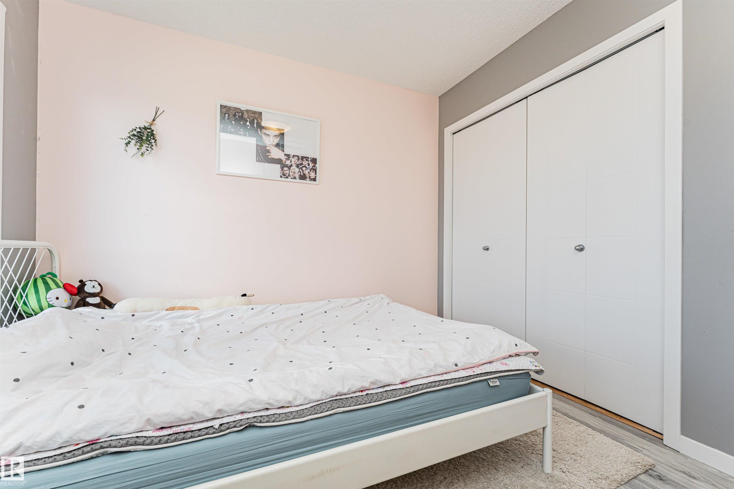 Bedroom featuring white bi-fold closet doors, light-toned wood-finish flooring, and a textured area rug - 4452 Annett Common, Edmonton, AB