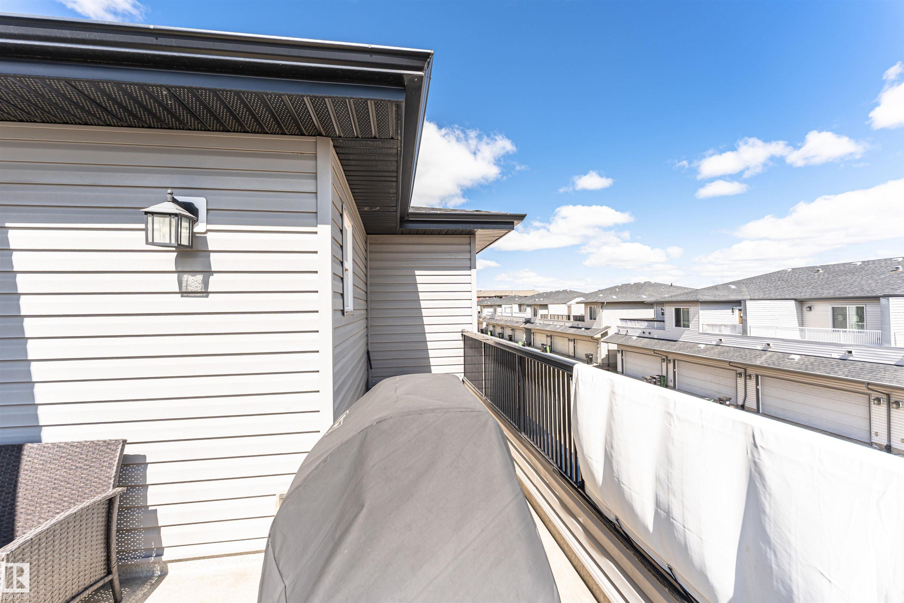 Exterior balcony featuring light-toned horizontal siding, a black metal railing, and an outdoor light fixture - 4452 Annett Common, Edmonton, AB