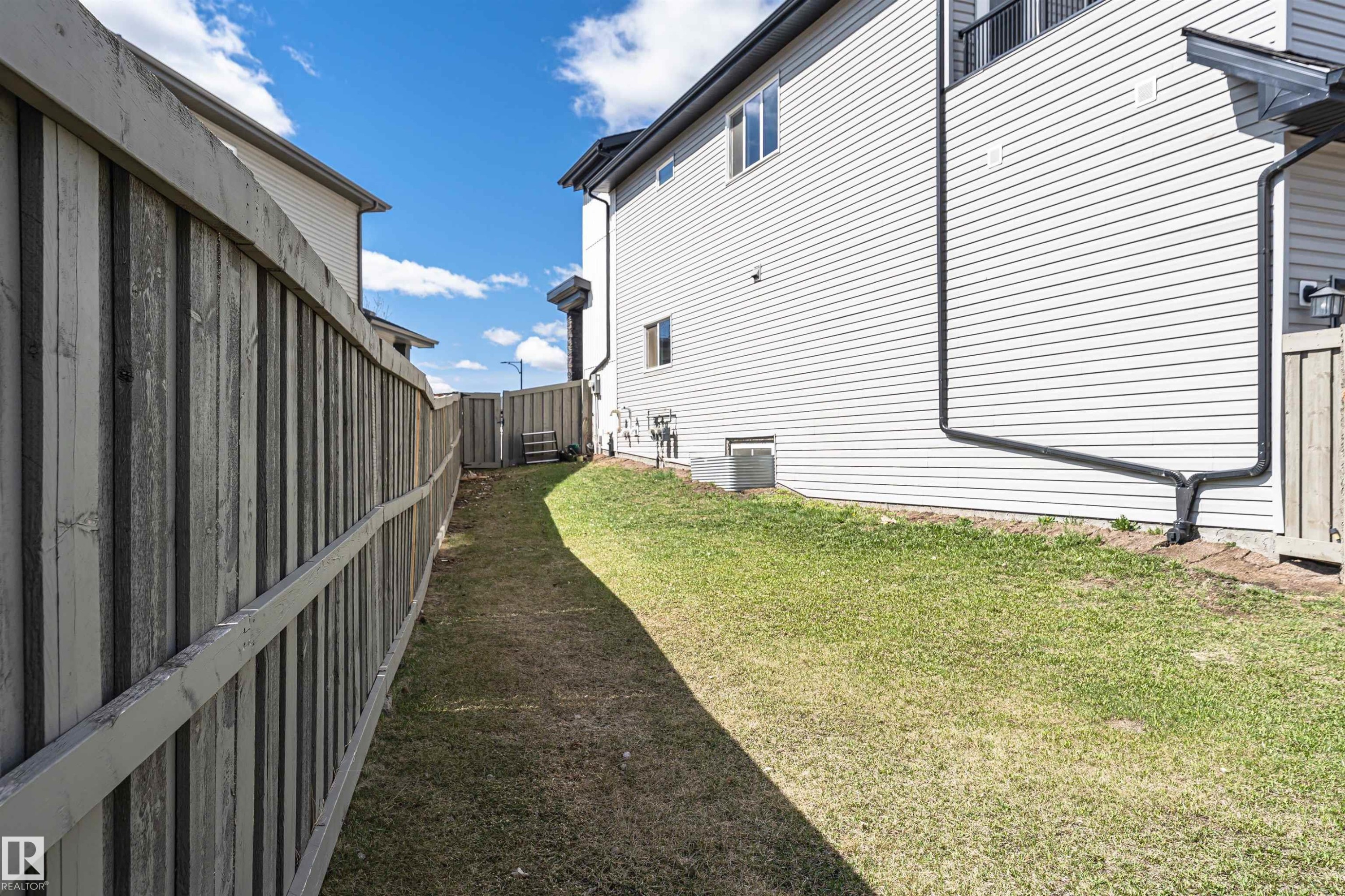 Side yard featuring a wooden privacy fence, green lawn, and vinyl siding exterior - 4452 Annett Common, Edmonton, AB
