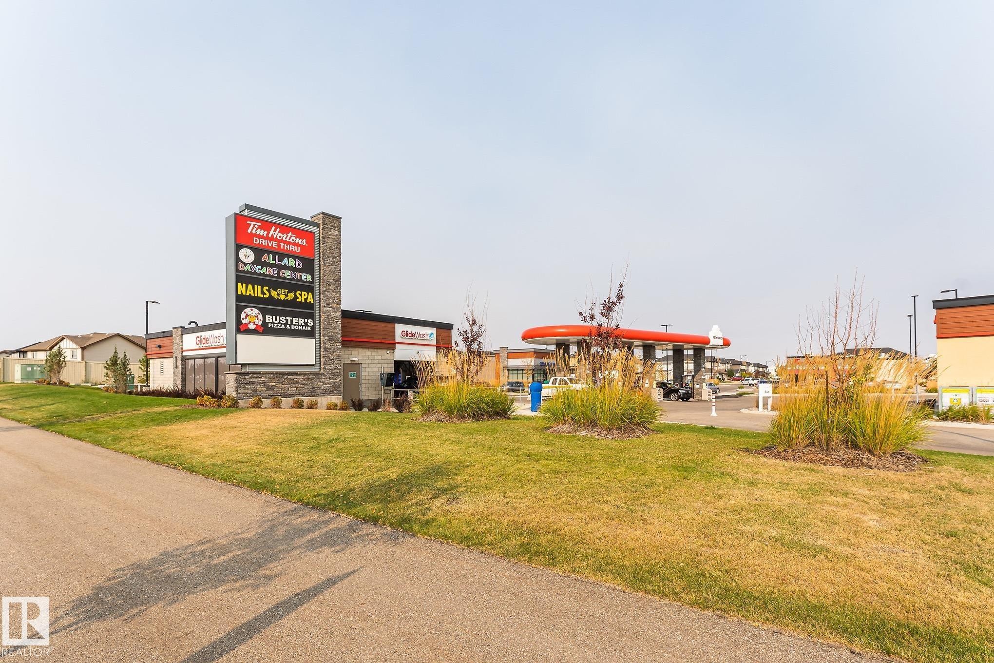 Retail center featuring a stone-clad pylon sign, a drive-thru building, a gas station canopy with red accents, and manicured landscaping - 4452 Annett Common, Edmonton, AB