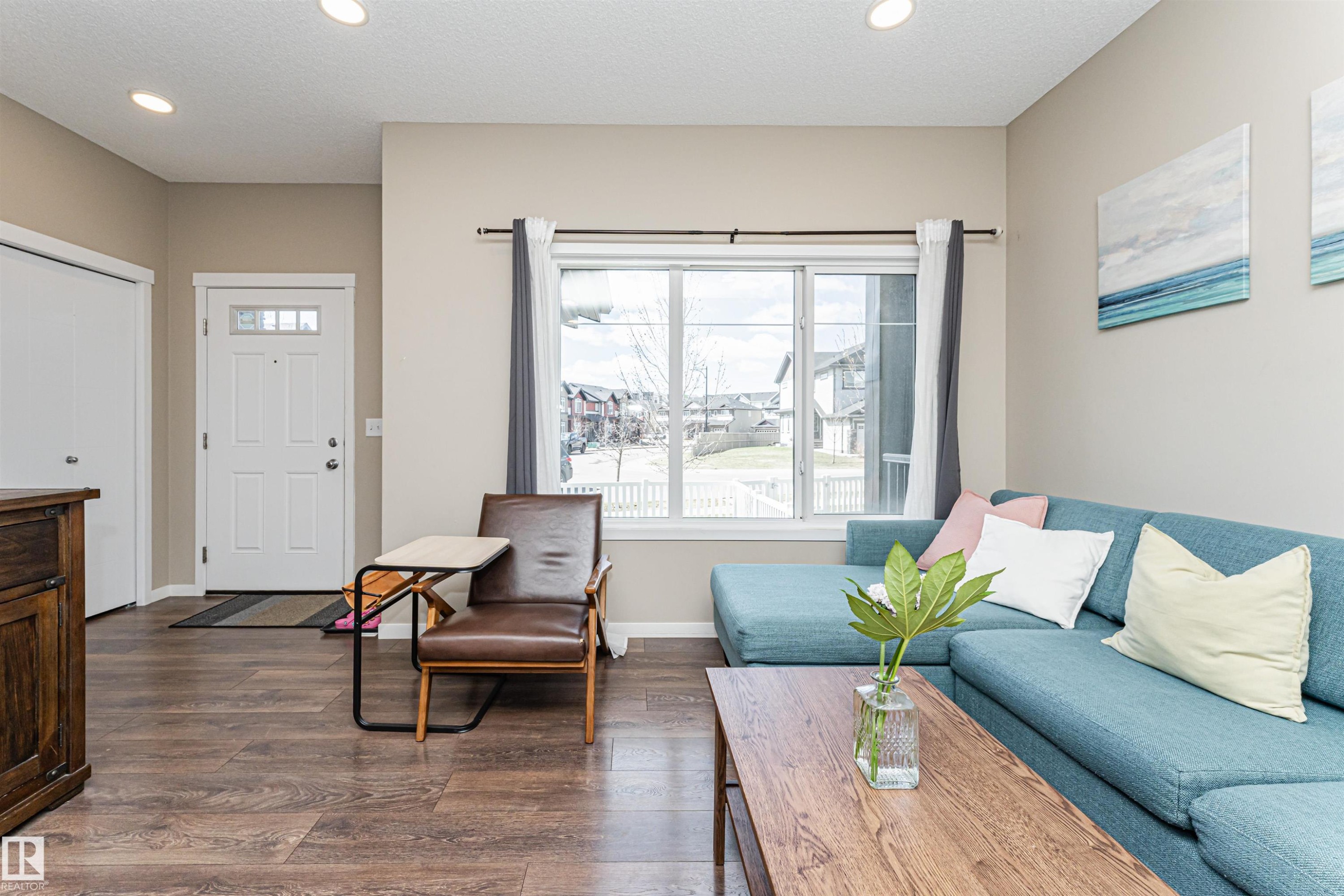 Open-concept living space with wood-finish flooring, a white paneled entry door with decorative glass inserts, and recessed ceiling lighting - 4452 Annett Common, Edmonton, AB