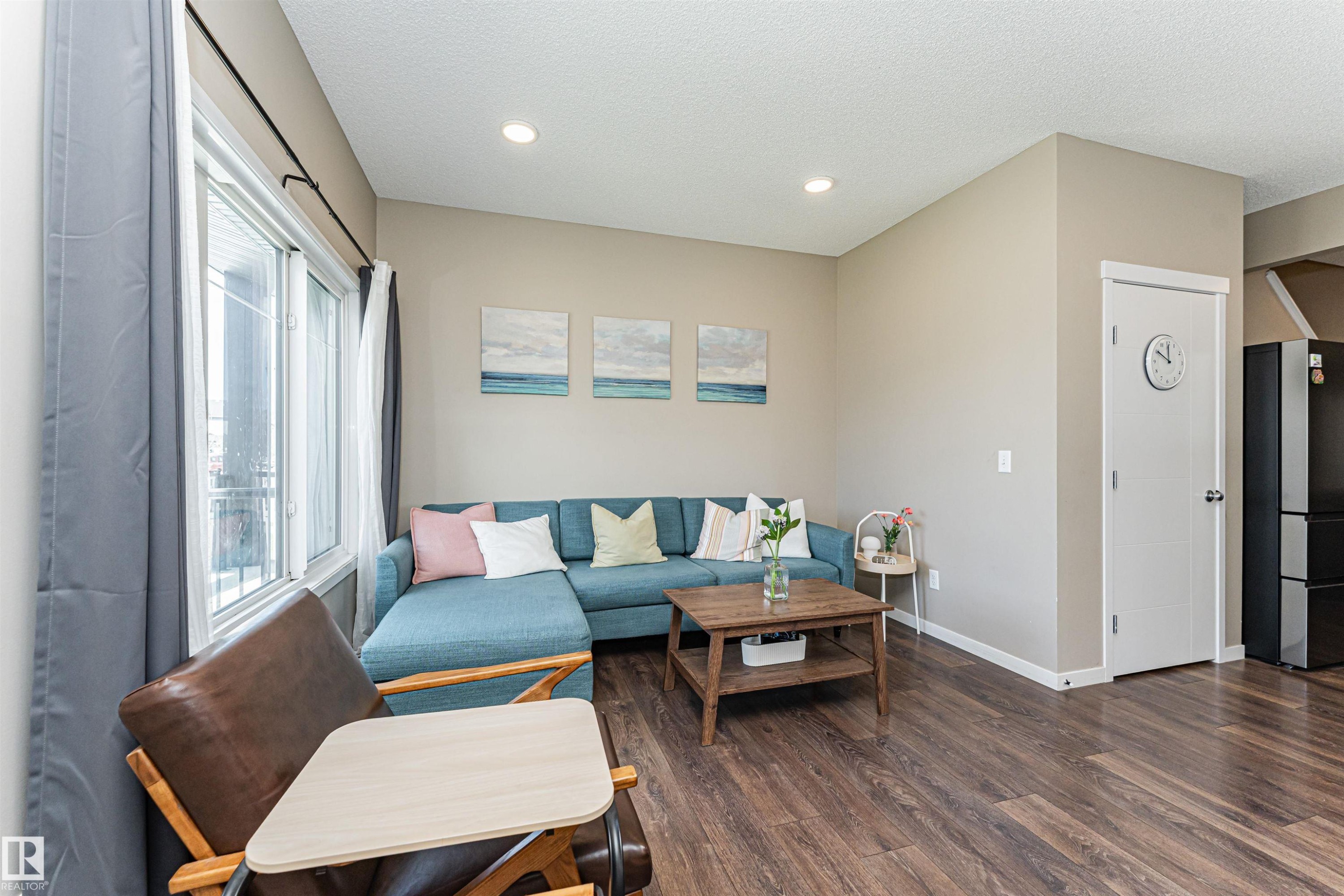 Living area featuring wood-finish flooring, recessed lighting, and a large window with white trim - 4452 Annett Common, Edmonton, AB