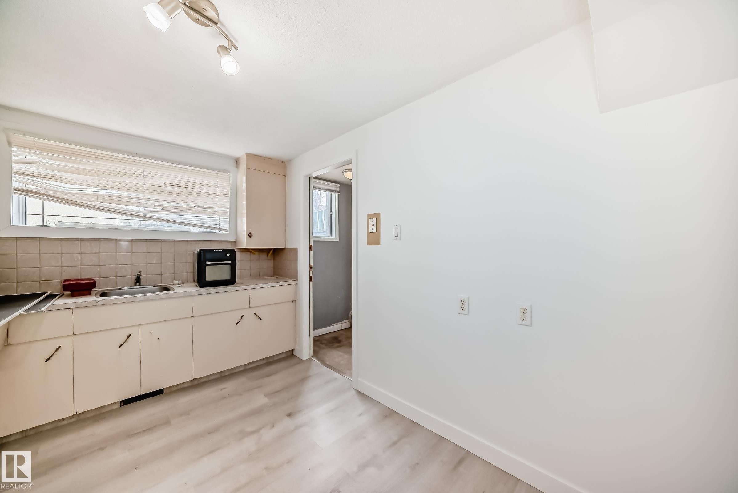 Kitchen area featuring light wood-finish flooring, track lighting, a window with horizontal blinds, a countertop with an integrated sink, and cabinetry - 12825 102 Street, Edmonton, AB - Indoor