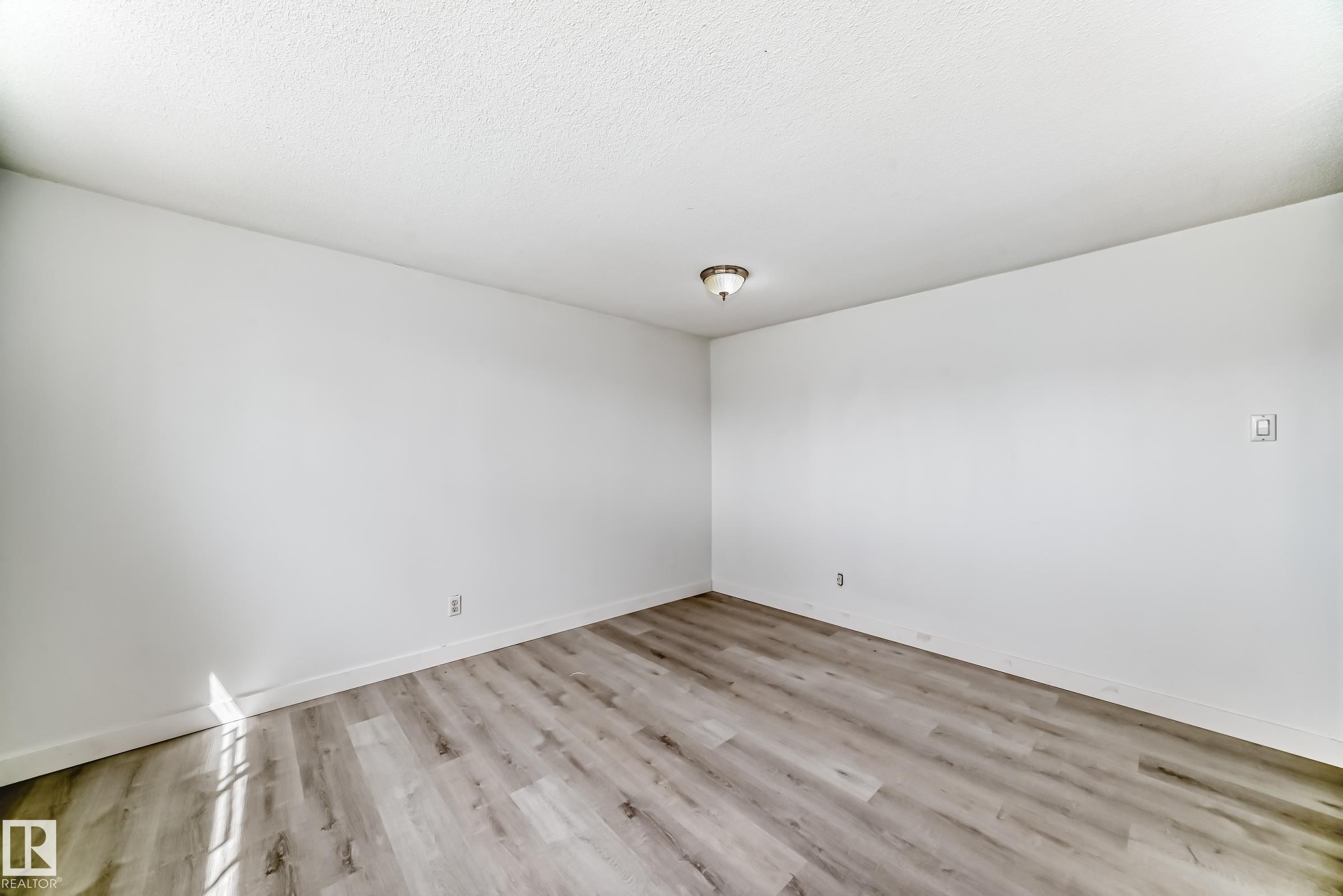 Room featuring wood-finish flooring, white walls, white baseboards, and a ceiling-mounted light fixture - 12825 102 Street, Edmonton, AB - Indoor Photo Showing Other Room