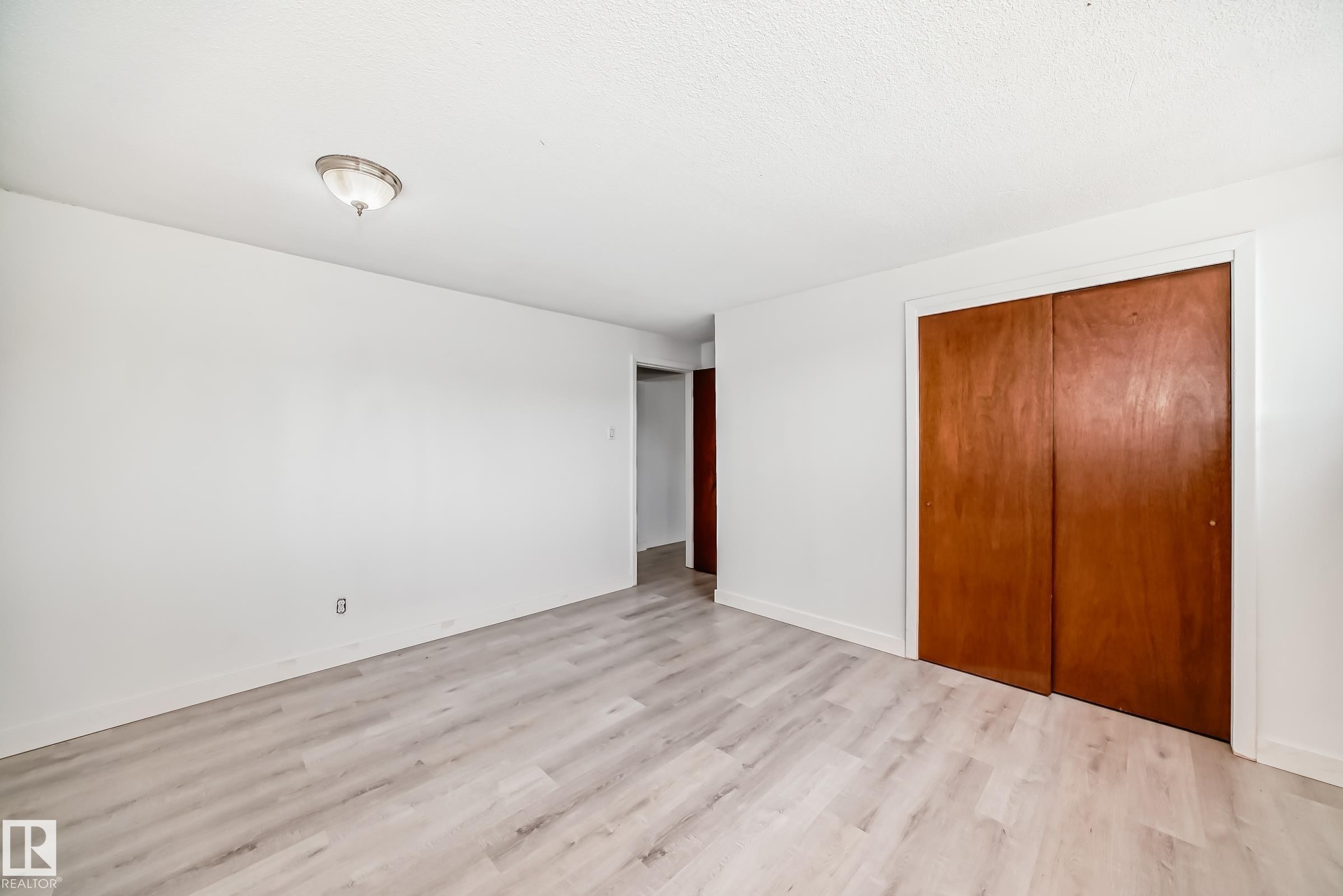 Light-toned wood-finish flooring complements white walls, featuring a flush-mount ceiling light and a built-in closet with warm wood bi-fold doors - 12825 102 Street, Edmonton, AB - Indoor Photo Showing Other Room
