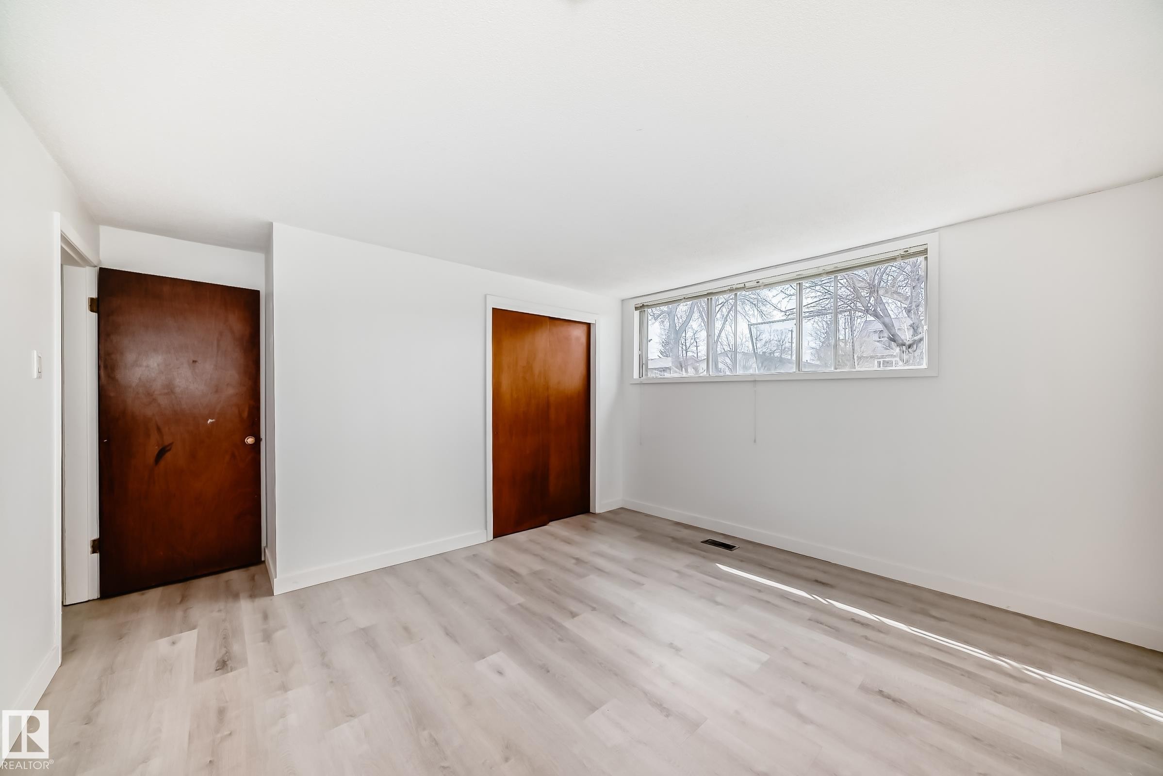 Bright interior space featuring light wood-finish flooring, white walls, and a wide window - 12825 102 Street, Edmonton, AB - Indoor Photo Showing Other Room