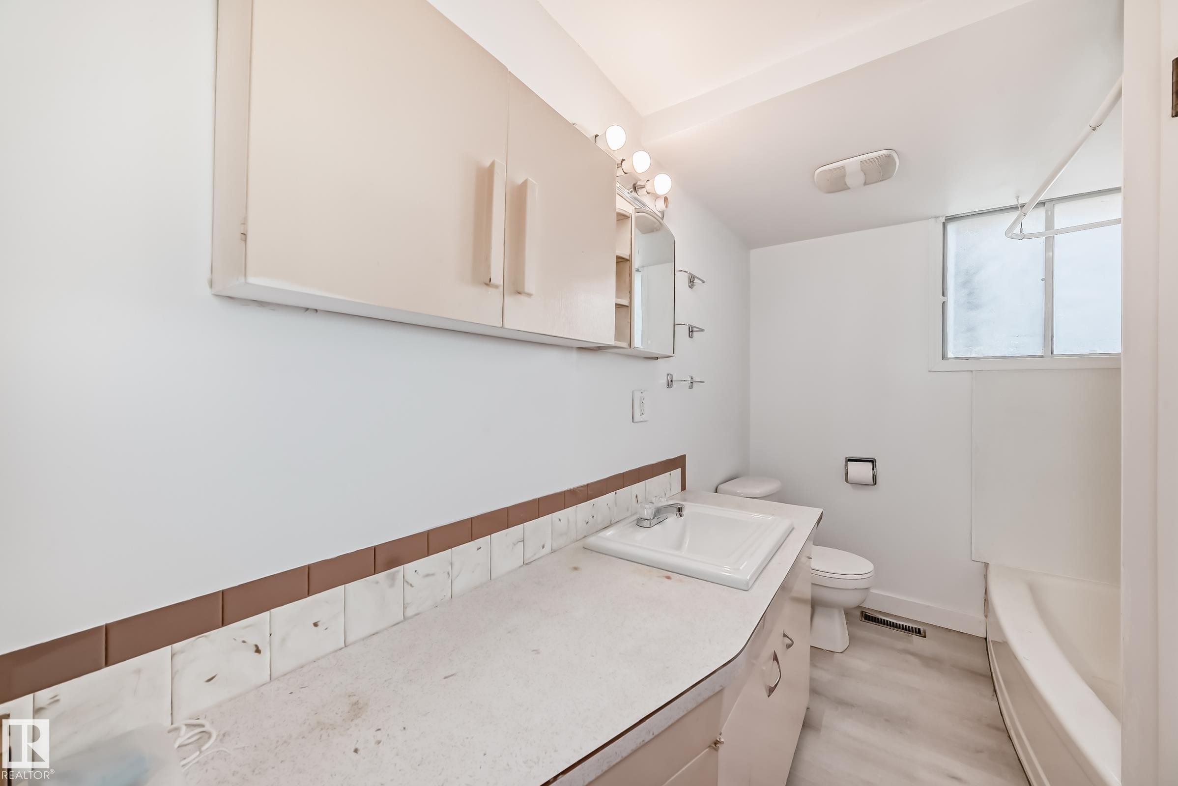 Bathroom featuring a single vanity with an integrated sink, overhead wall cabinets, and a bathtub with shower - 12825 102 Street, Edmonton, AB - Indoor Photo Showing Laundry Room