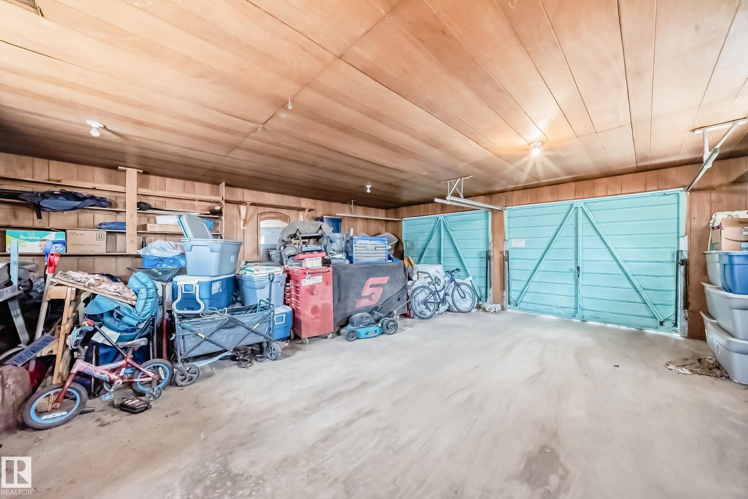 Garage space featuring two light blue double doors, wood paneling on walls and ceiling, and exposed ceiling light fixtures - 12825 102 Street, Edmonton, AB - Indoor Photo Showing Garage