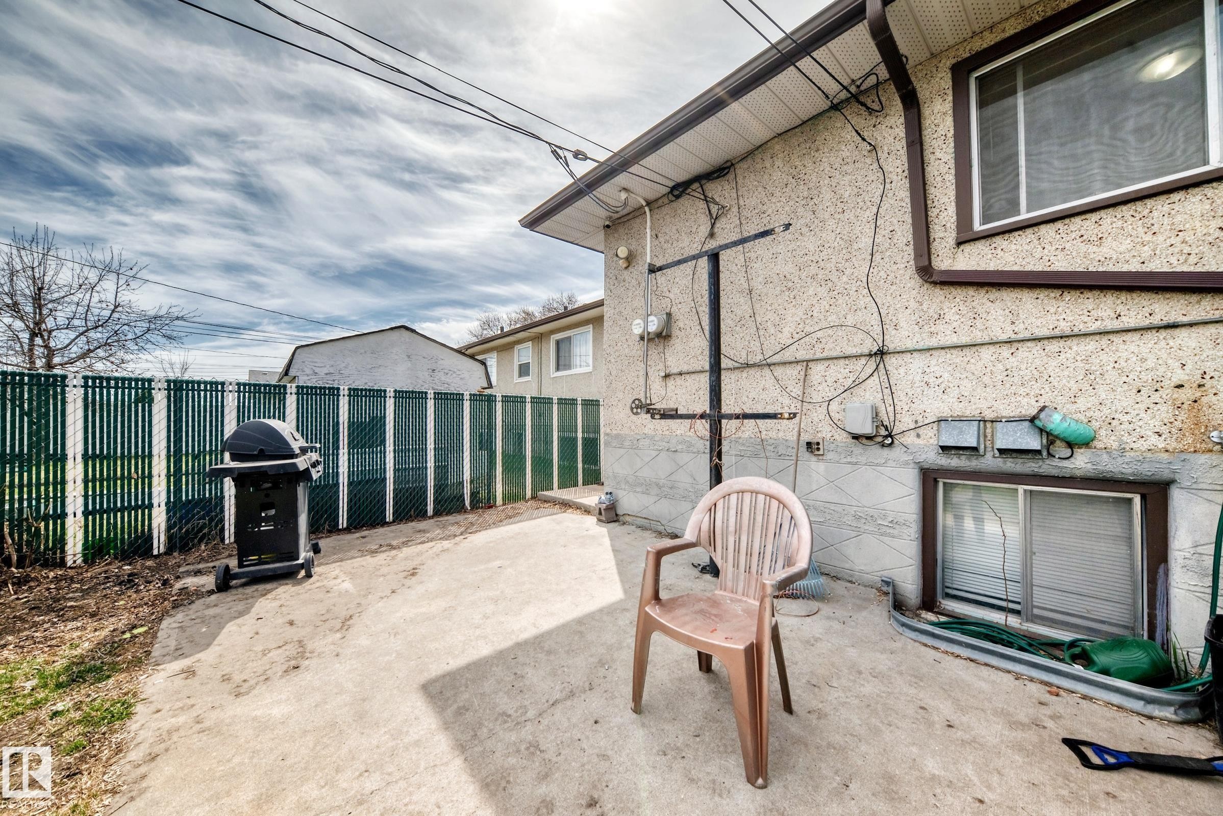 Exterior concrete patio with a full-height green privacy fence - 12825 102 Street, Edmonton, AB - Outdoor With Exterior