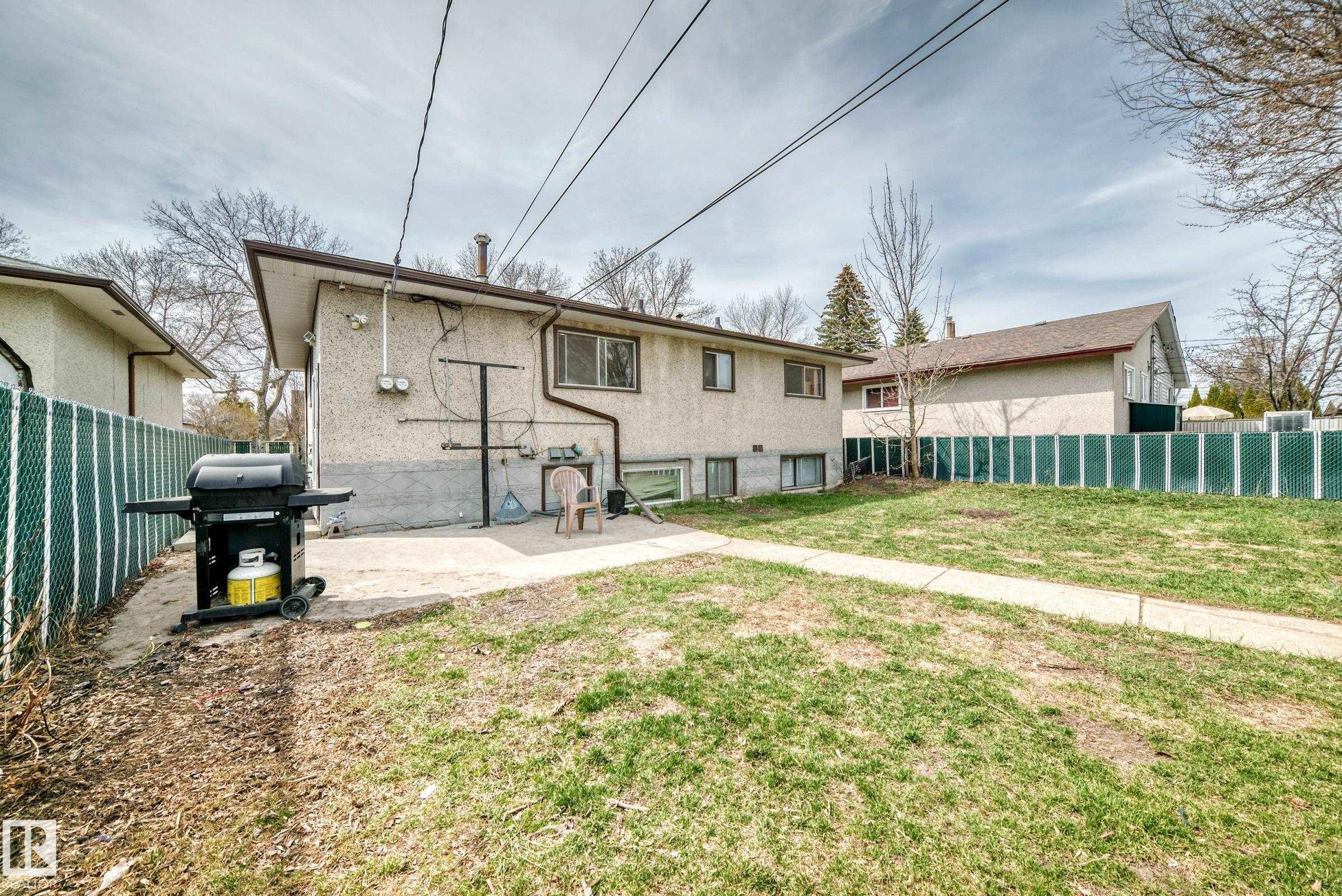 Spacious backyard featuring a chain-link fence, concrete patio, and mature trees - 12825 102 Street, Edmonton, AB - Outdoor With Exterior