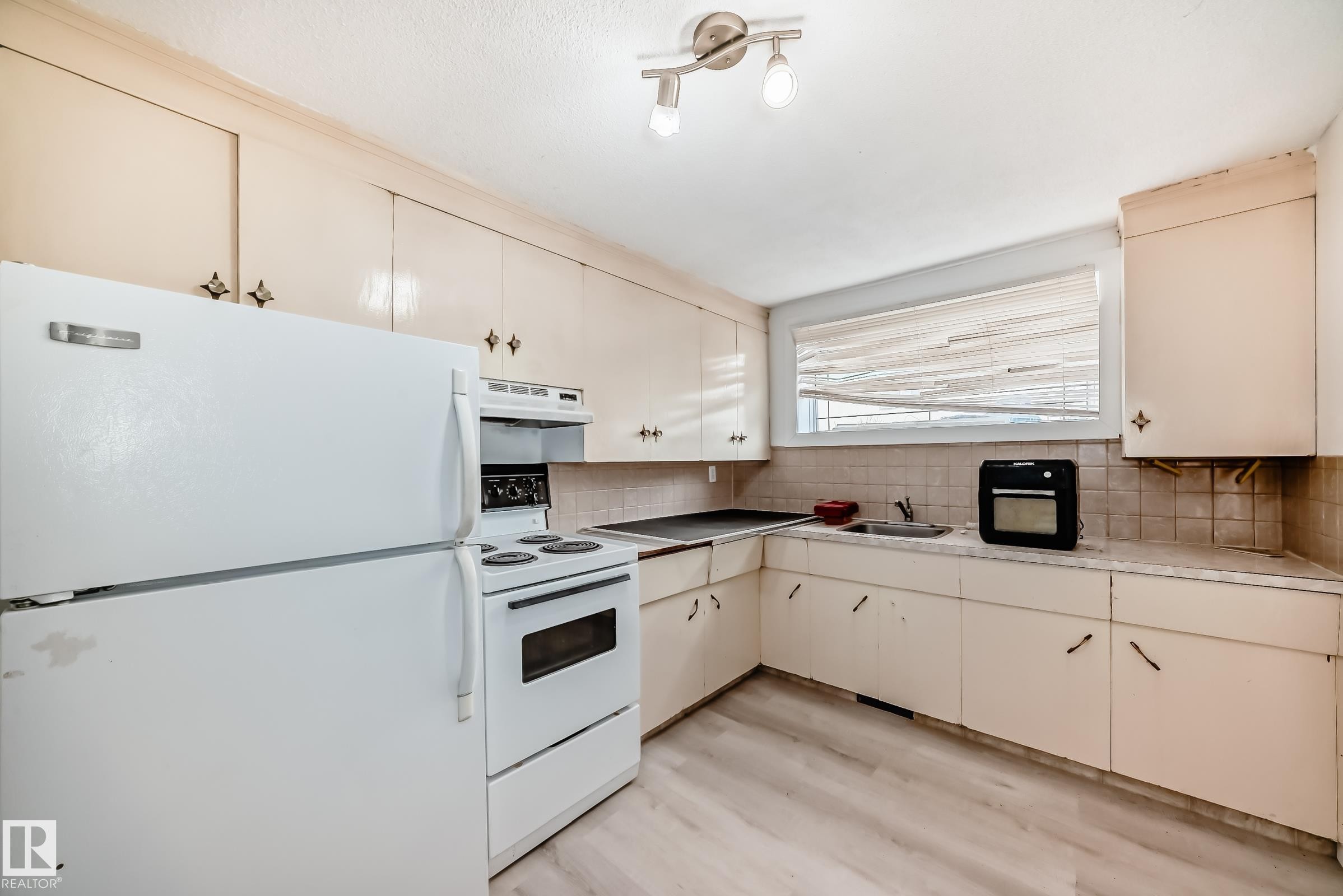 Kitchen featuring ample cabinetry, white appliance suite, a sink, a window with blinds, and light wood-finish flooring - 12825 102 Street, Edmonton, AB - Indoor Photo Showing Kitchen