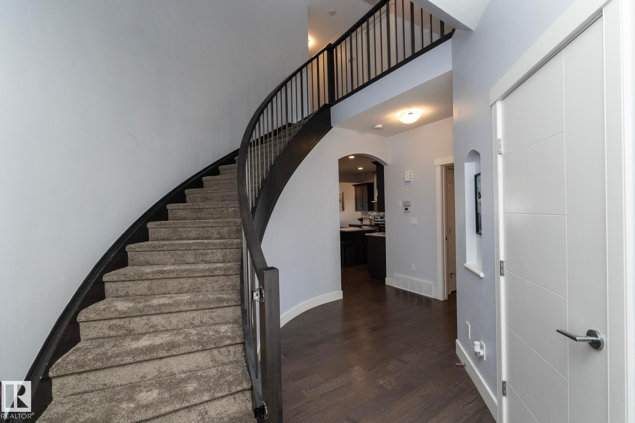 Curved staircase with dark wood-finish handrail and carpeted treads - 2016 Redtail Common, Edmonton, AB - Indoor Photo Showing Other Room