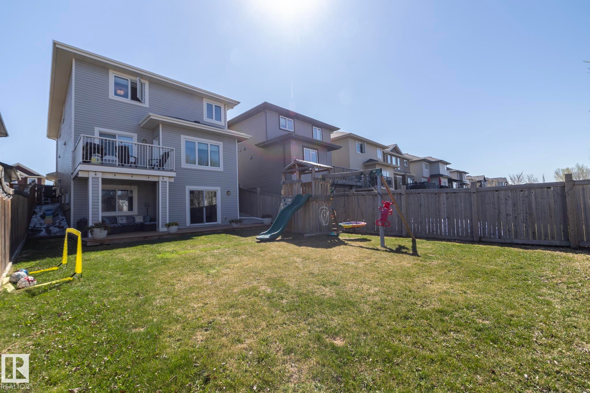 Spacious fenced backyard featuring a manicured lawn, an elevated deck with black metal railings, and a ground-level patio - 2016 Redtail Common, Edmonton, AB - Outdoor