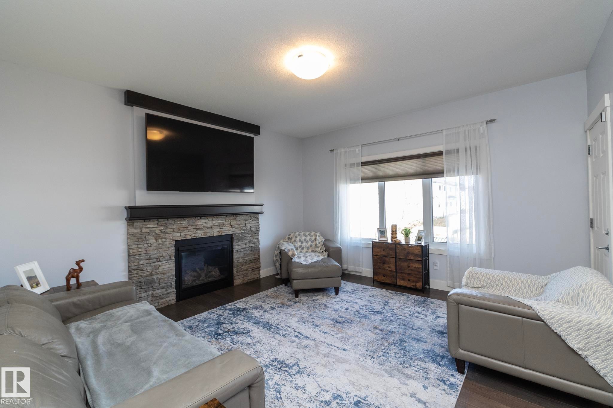 Living area featuring a stone-faced fireplace with a dark wood mantel, recessed gas insert, and dark wood-finish flooring - 2016 Redtail Common, Edmonton, AB - Indoor Photo Showing Living Room With Fireplace