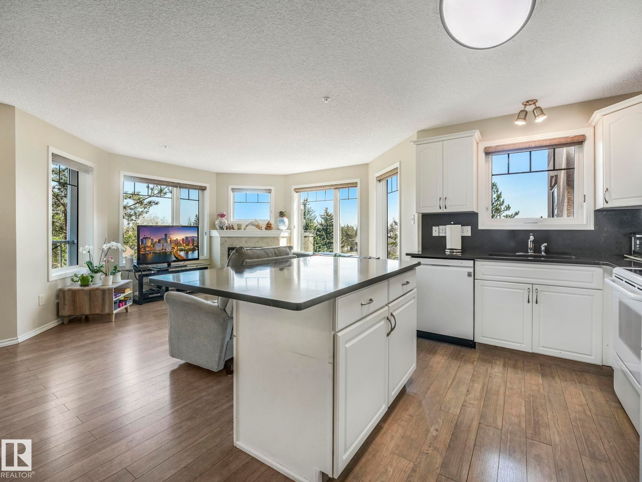 Open-concept living area featuring a kitchen island with dark countertops, white cabinetry, integrated appliances, and wood-finish flooring throughout - 317 2420 108 Street, Edmonton, AB - Indoor Photo Showing Kitchen