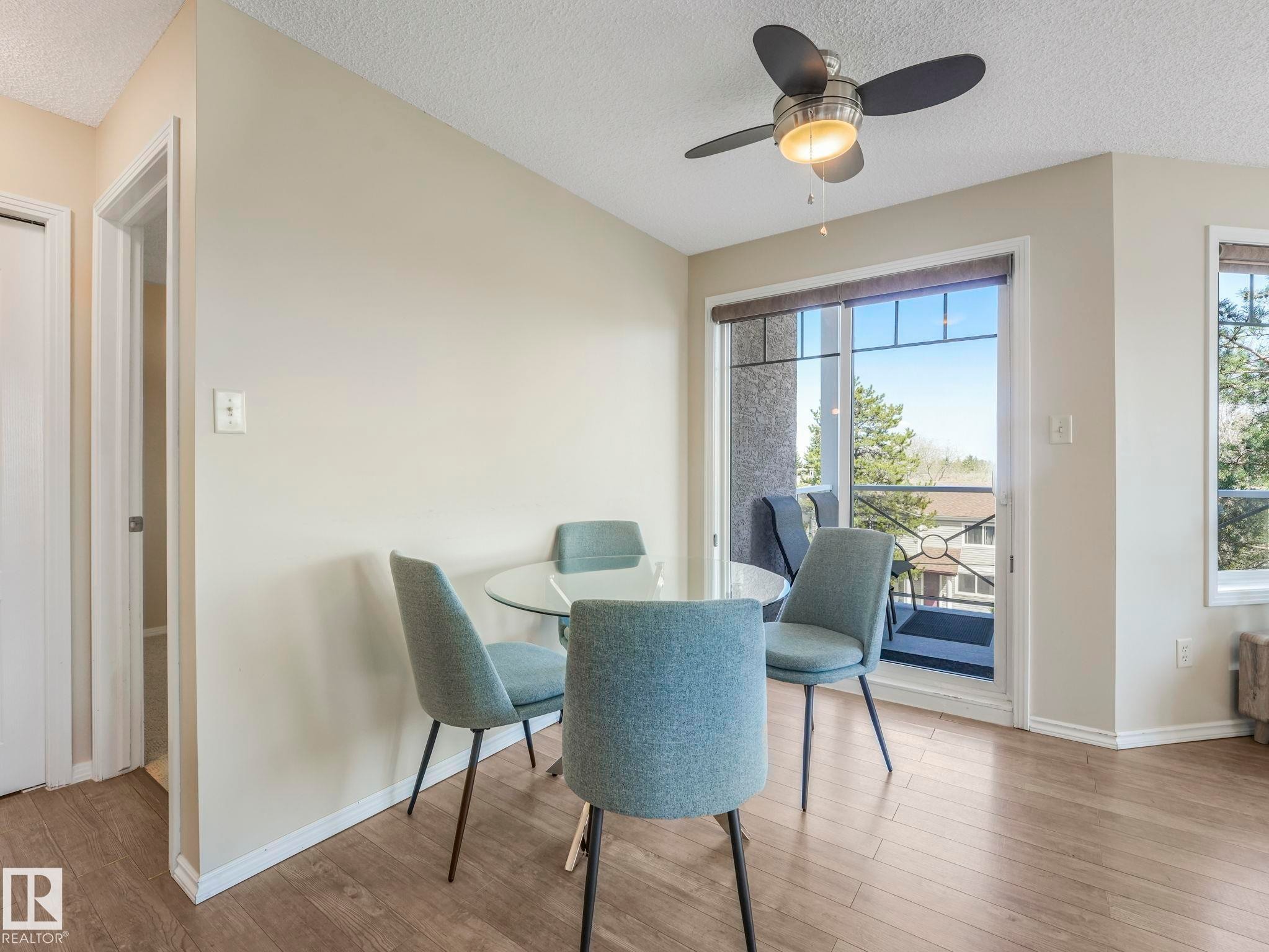 Bright interior space with wood-finish flooring, a ceiling fan with integrated lighting, and a sliding glass door providing balcony access - 317 2420 108 Street, Edmonton, AB - Indoor Photo Showing Dining Room