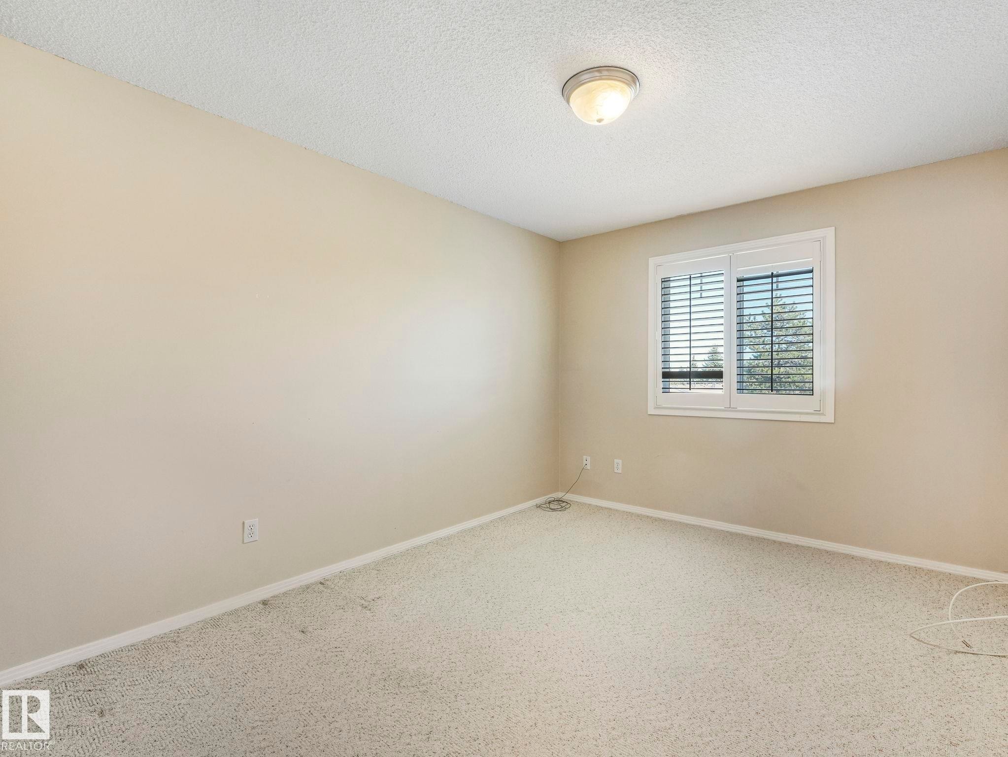 Neutral-toned bedroom featuring wall-to-wall carpeting, a multi-pane window with horizontal blinds, and a semi-flush mount ceiling light fixture - 317 2420 108 Street, Edmonton, AB - Indoor Photo Showing Other Room