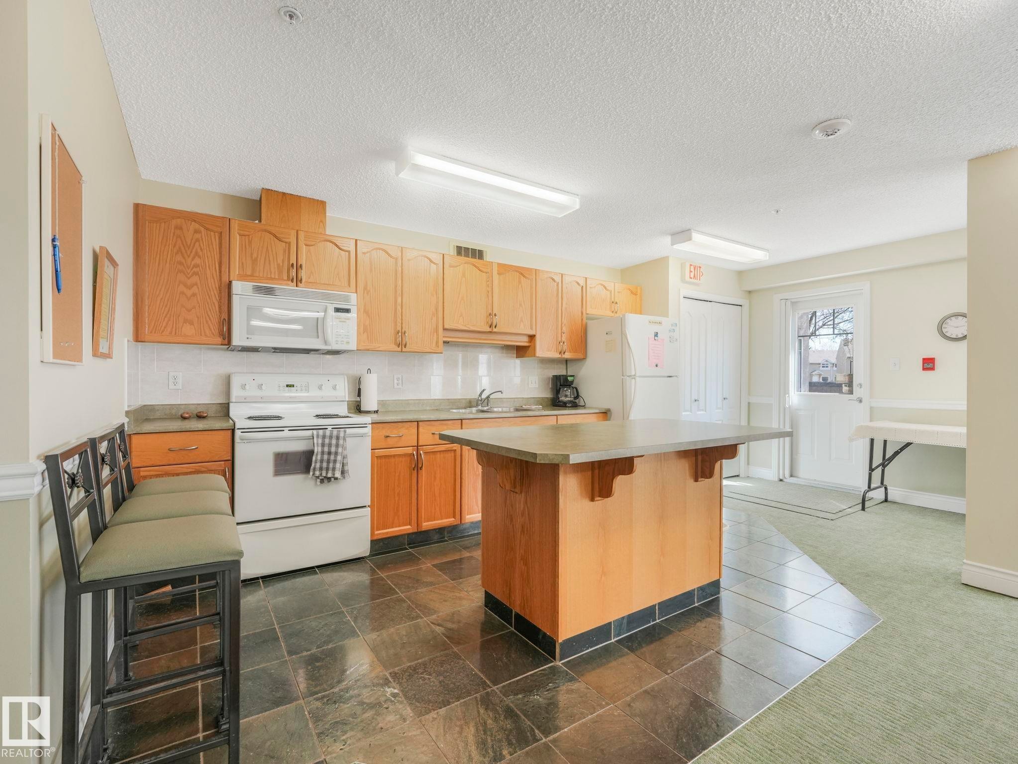 Kitchen space featuring full-height wood cabinetry, white tile backsplash, and a central island with a stone-finish countertop - 317 2420 108 Street, Edmonton, AB - Indoor Photo Showing Kitchen