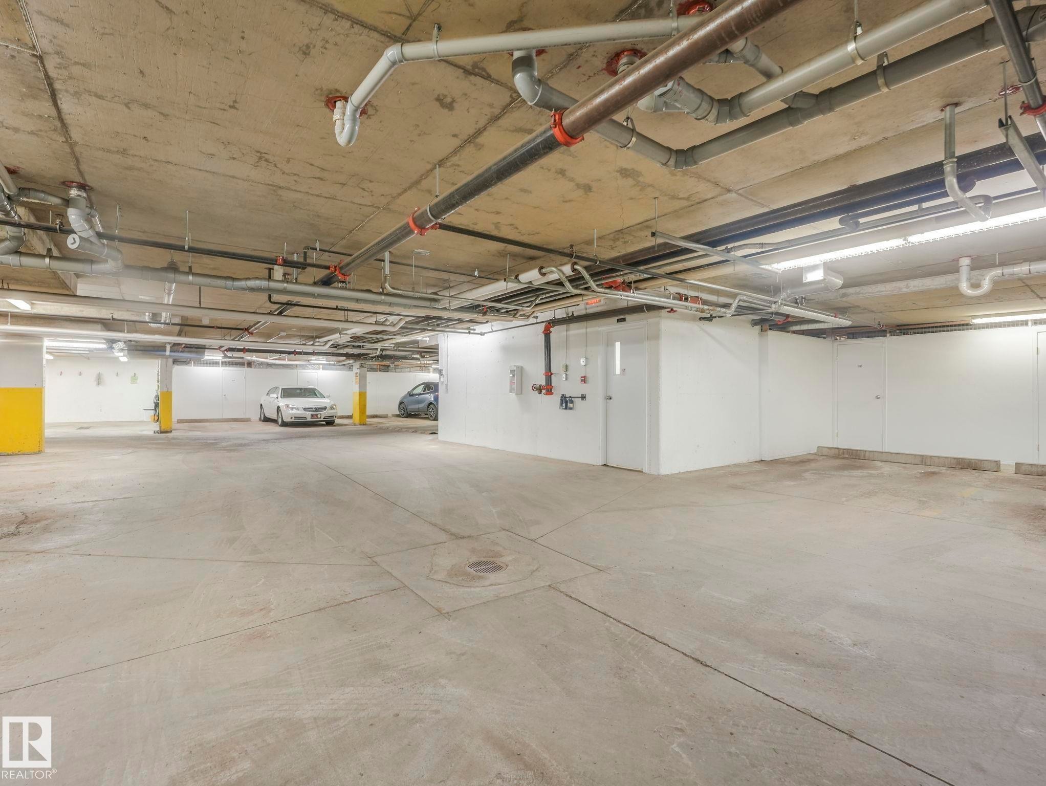 Underground parking garage featuring concrete flooring and ceiling, exposed utility piping, fluorescent strip lighting, and yellow-painted support columns - 317 2420 108 Street, Edmonton, AB - Indoor Photo Showing Garage