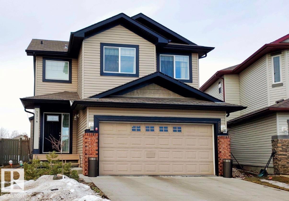Two-story residence featuring light beige siding with dark trim, an attached garage, brick accents, and a covered entry - 3214 22A Avenue, Edmonton, AB - Outdoor