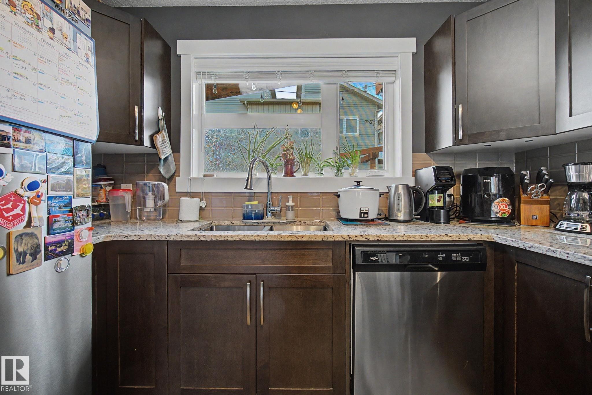 Kitchen featuring dark wood-finish cabinetry, light speckled countertops, and a tiled backsplash - 210 401 Southfork Drive, Leduc, AB - Indoor Photo Showing Kitchen With Double Sink
