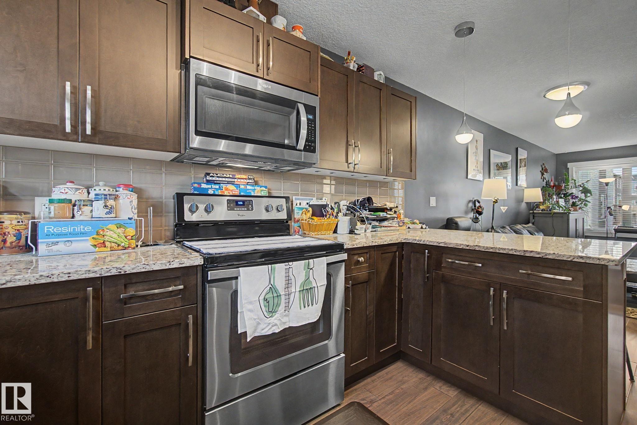 Kitchen featuring wood-finish cabinetry, light-toned countertops, tile backsplash, and stainless steel appliances - 210 401 Southfork Drive, Leduc, AB - Indoor Photo Showing Kitchen With Upgraded Kitchen