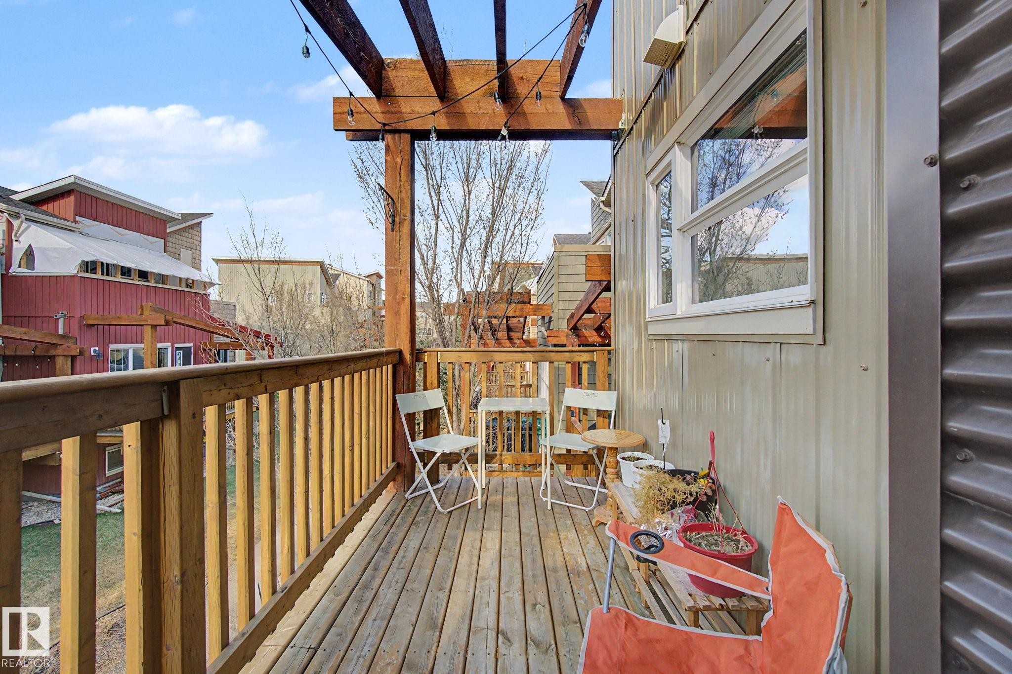 Wood-plank balcony featuring a wooden railing, overhead pergola, and string lighting - 210 401 Southfork Drive, Leduc, AB - Outdoor With Deck Patio Veranda With Exterior