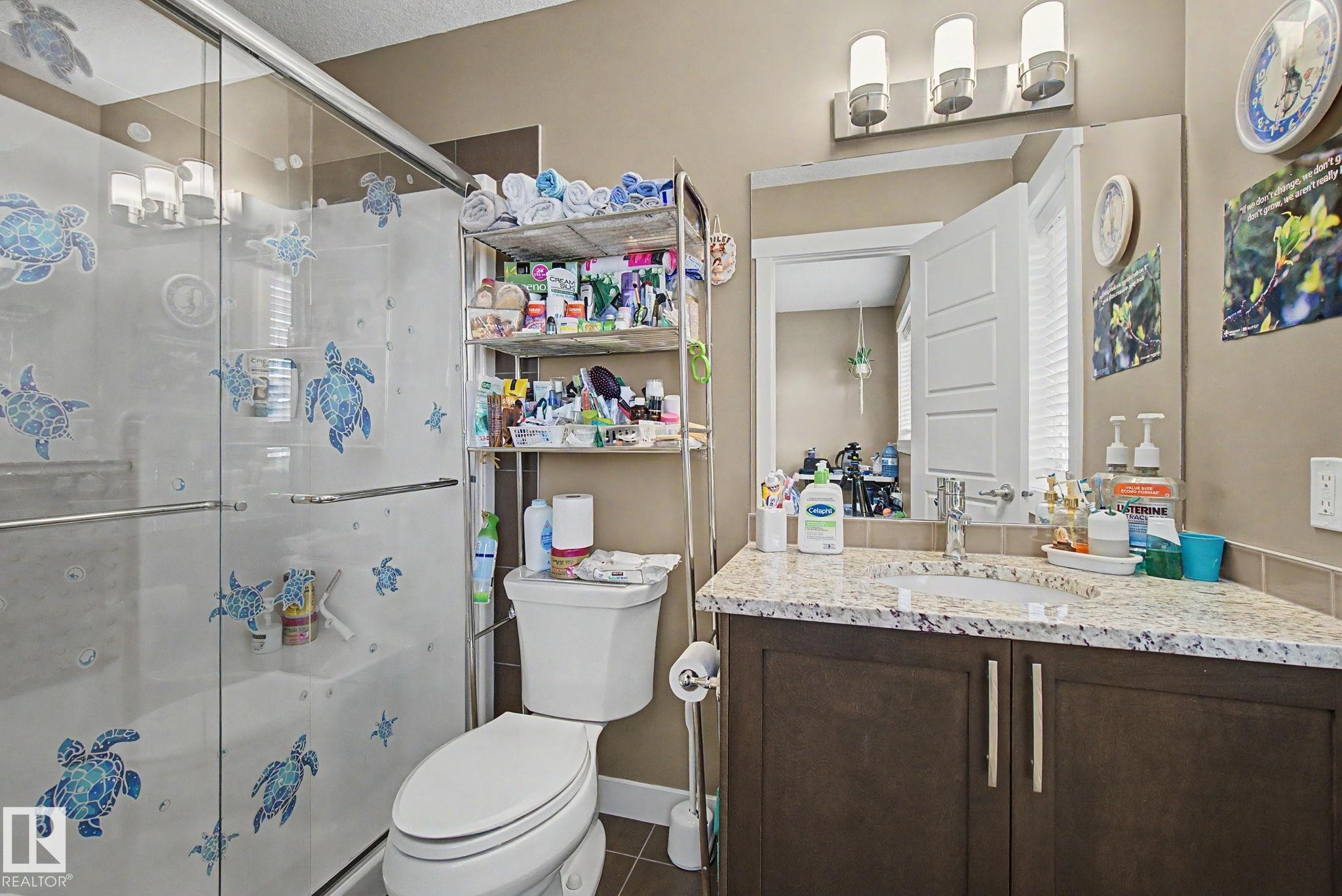 Bathroom featuring a glass-enclosed shower, a vanity with a white countertop and integrated sink, a dark wood-finish cabinet, and a wall-mounted light fixture above a mirror - 210 401 Southfork Drive, Leduc, AB - Indoor Photo Showing Bathroom