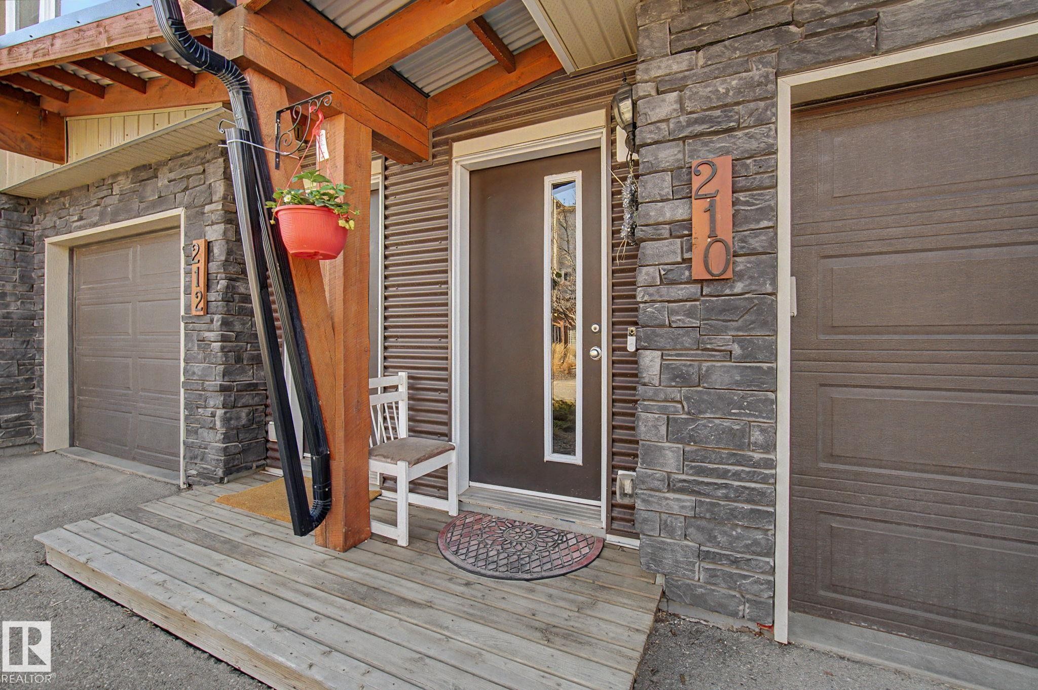 Wood-finish entry deck leading to a dark brown entry door with vertical window panel - 210 401 Southfork Drive, Leduc, AB - Outdoor With Exterior