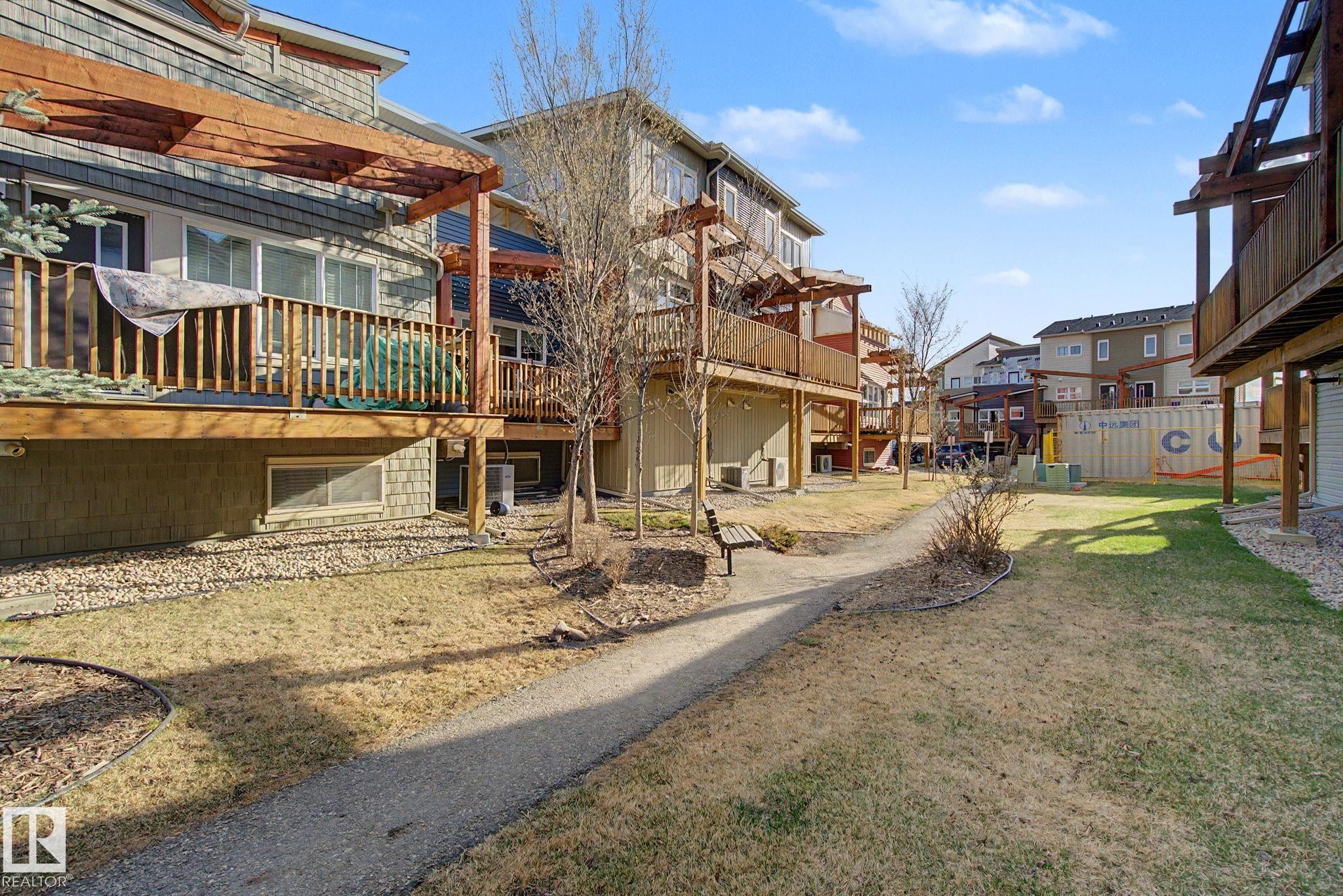 Community green space with a gravel pathway, complemented by mature trees and a dedicated bench area - 210 401 Southfork Drive, Leduc, AB - Outdoor