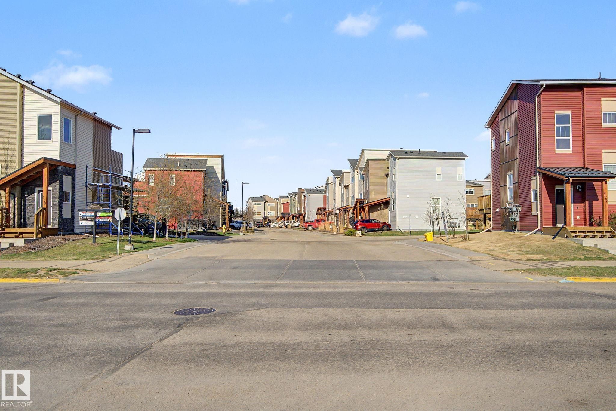 Residential street lined with multi-story townhomes featuring varied siding colors and architectural styles - 210 401 Southfork Drive, Leduc, AB - Outdoor