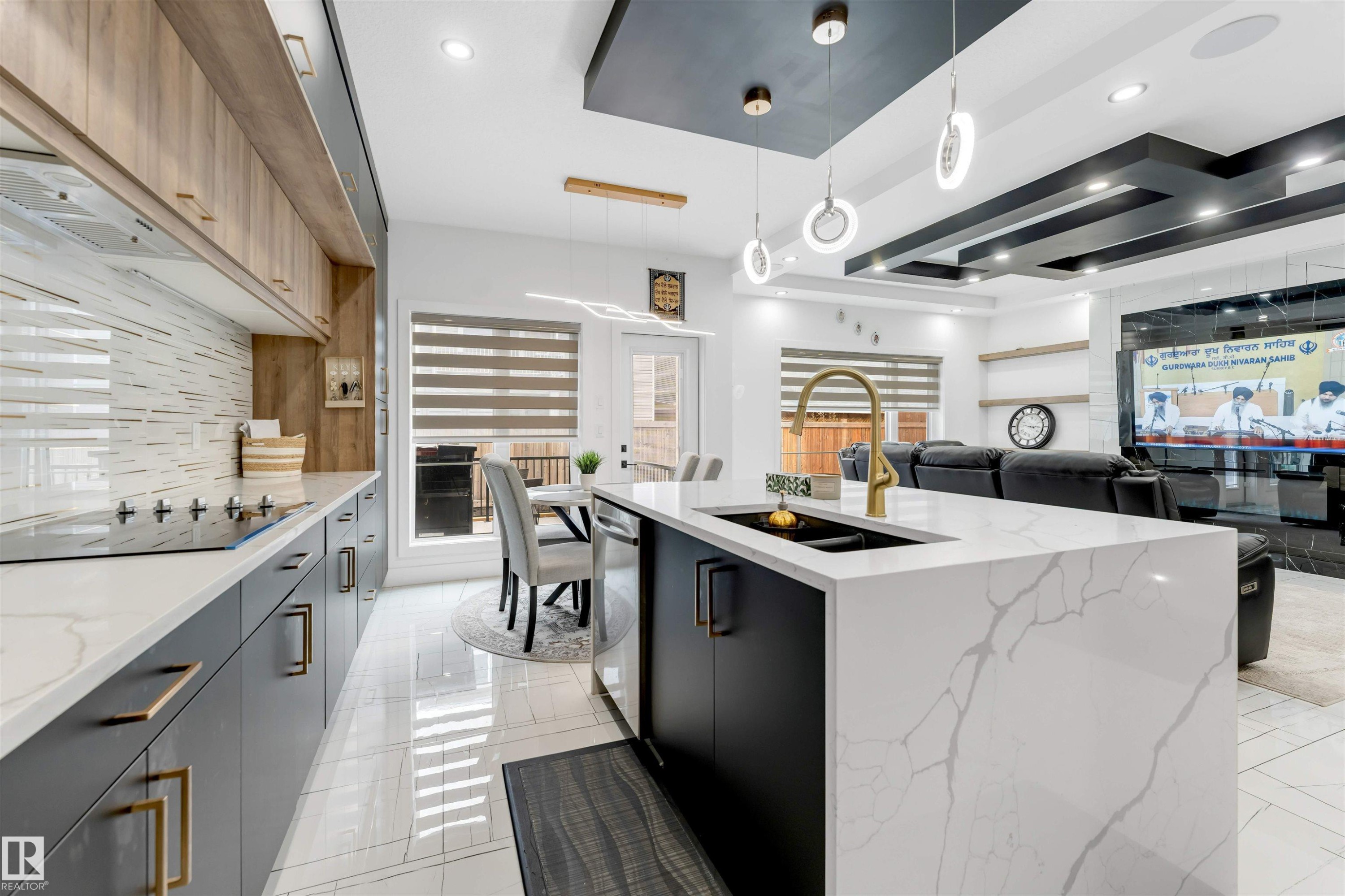 Open-concept kitchen featuring a waterfall island with an undermount sink and gold-finish faucet, integrated cooktop, wood-finish upper cabinetry, and a patterned tile backsplash - 1827 17 Avenue, Edmonton, AB - Indoor Photo Showing Kitchen With Upgraded Kitchen