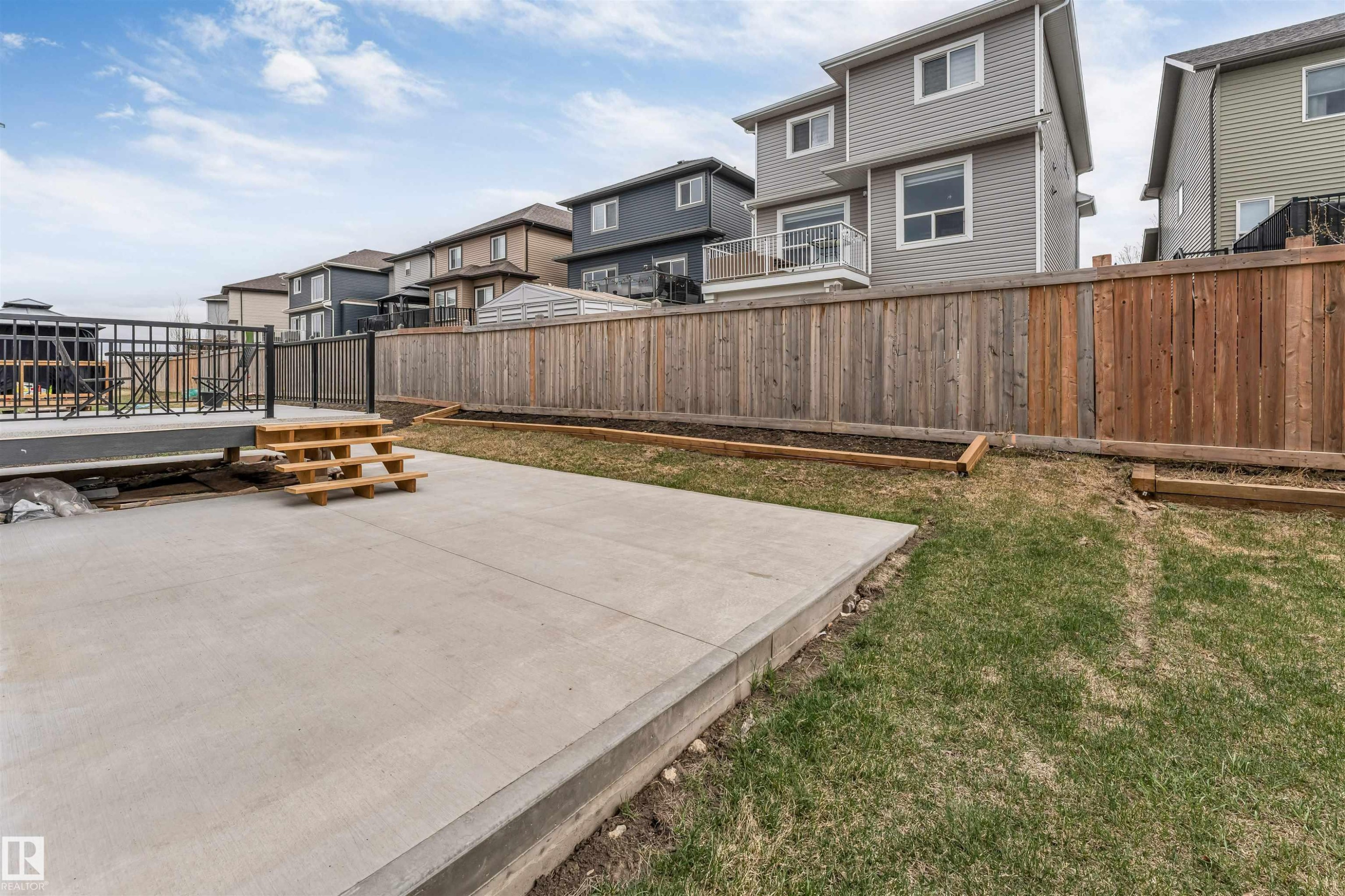 Expansive concrete patio with integrated steps leading to an elevated deck featuring black metal railings - 1827 17 Avenue, Edmonton, AB - Outdoor