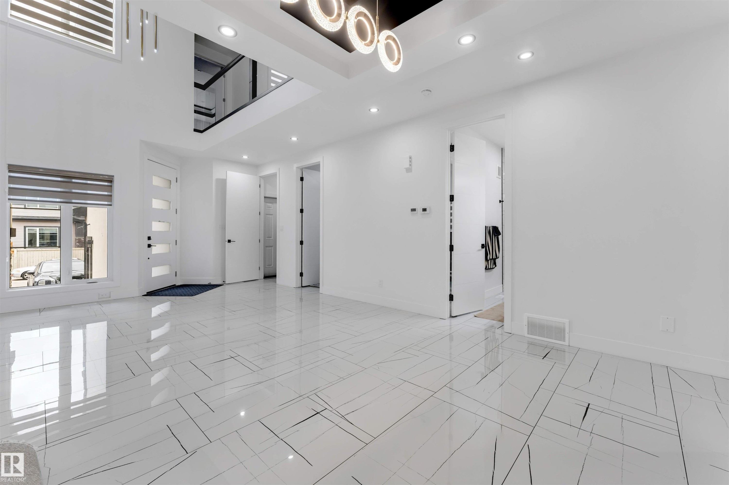Spacious interior featuring high ceilings, contemporary white tile flooring with linear accents, recessed lighting, and a modern chandelier - 1827 17 Avenue, Edmonton, AB - Indoor Photo Showing Other Room