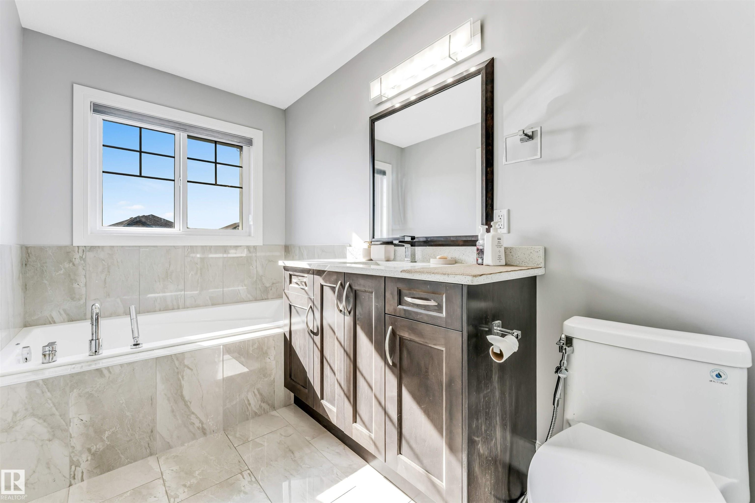 Bathroom featuring a built-in tub with tile surround, a single vanity with stone countertop, and a large framed mirror - 1103 29 Street, Edmonton, AB - Indoor Photo Showing Bathroom