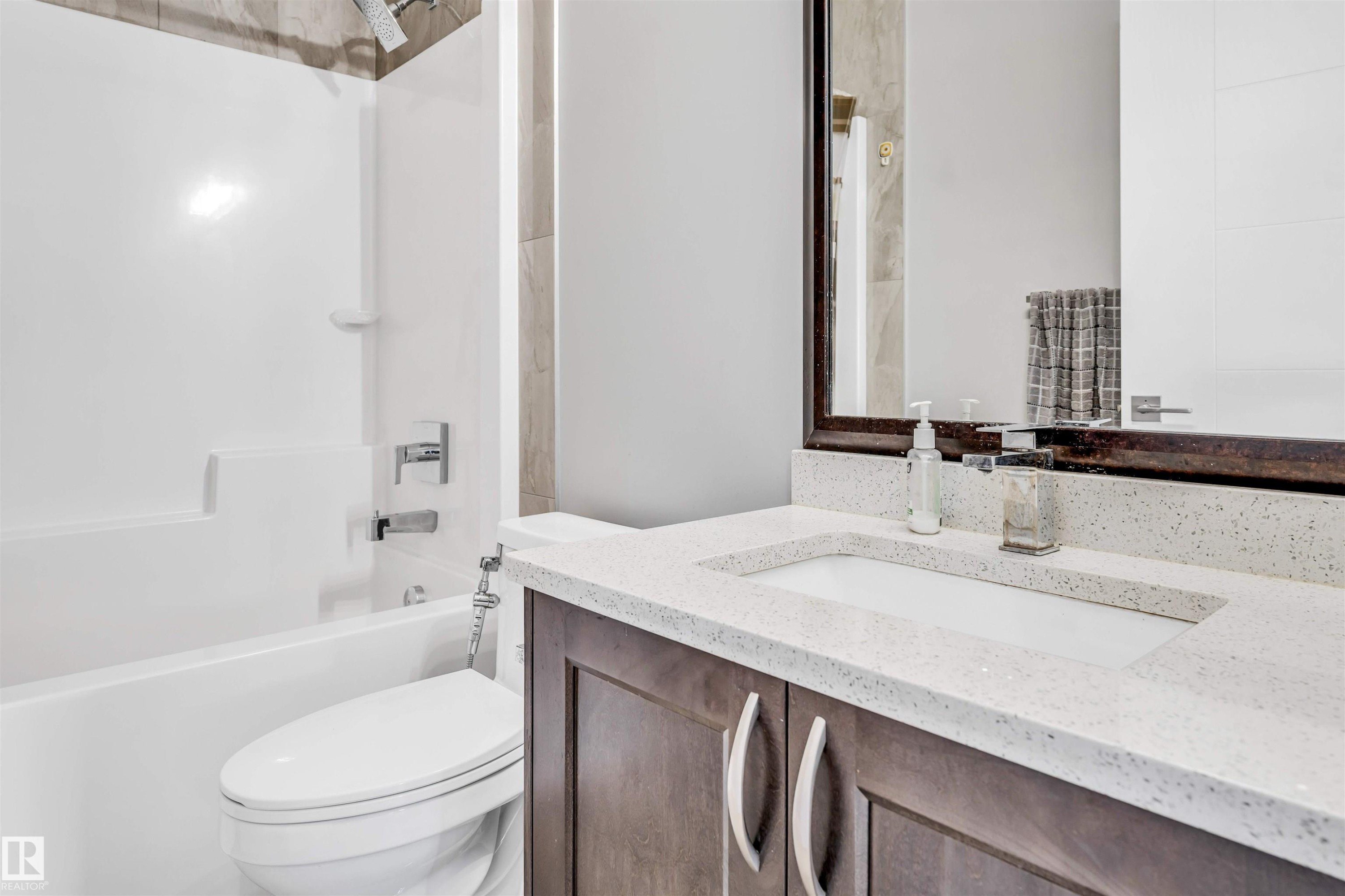 Bathroom featuring a dark wood vanity with a white composite countertop, an integrated rectangular sink, a framed mirror, and a white tub with a shower combo - 1103 29 Street, Edmonton, AB - Indoor Photo Showing Bathroom