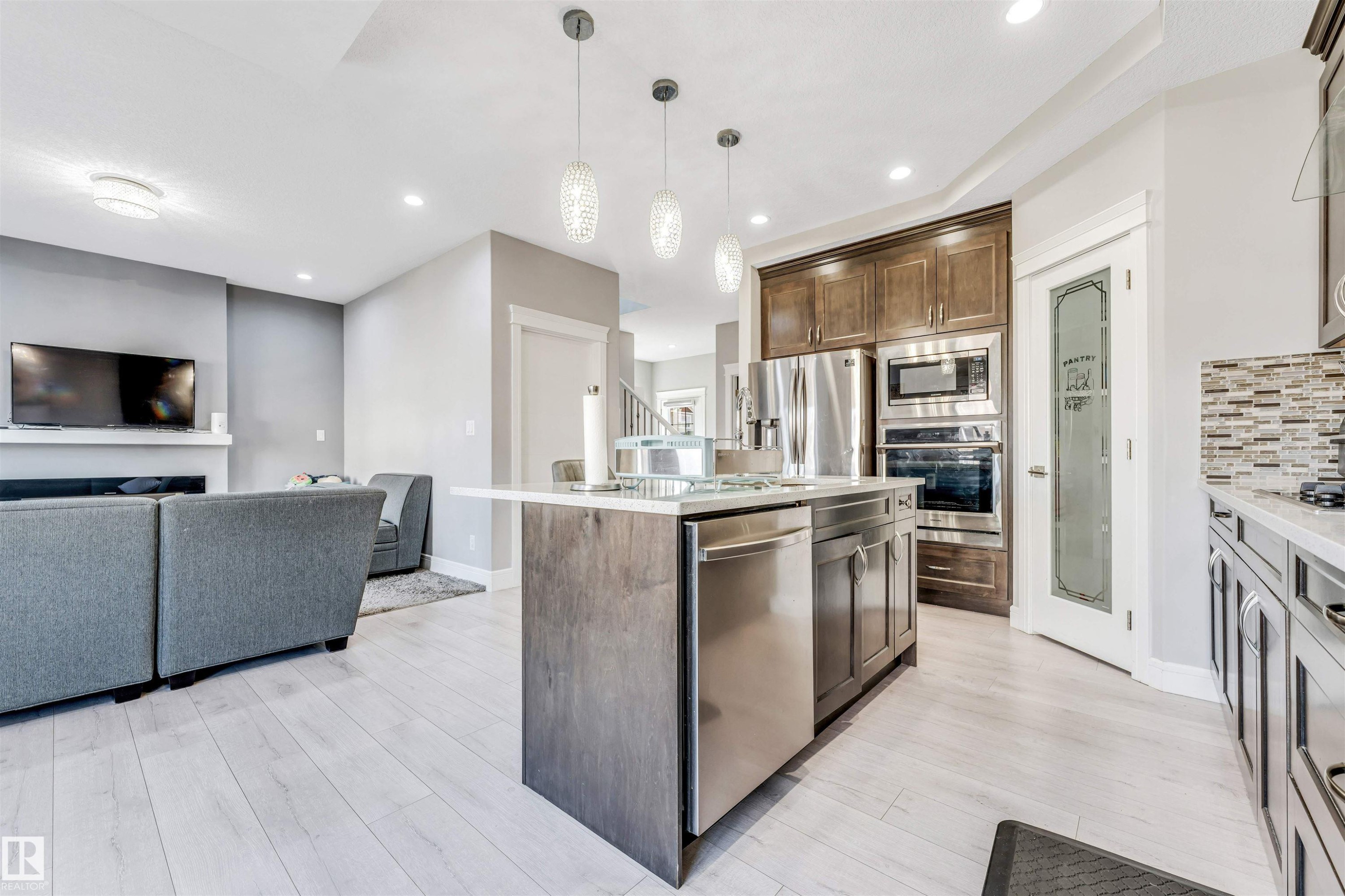 Open-concept kitchen featuring an island with pendant lighting, stainless steel appliances, wood-finish flooring, and a pantry with a frosted glass door - 1103 29 Street, Edmonton, AB - Indoor Photo Showing Kitchen With Upgraded Kitchen