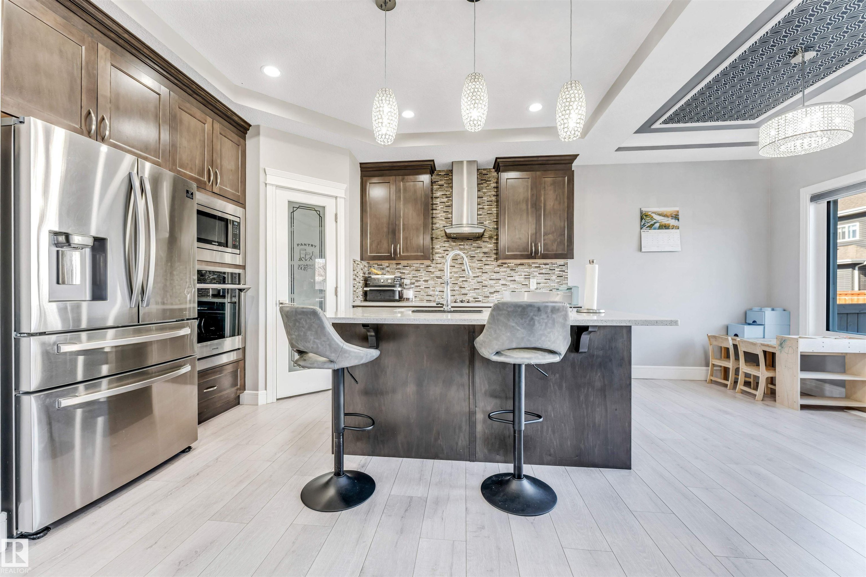 Gourmet kitchen featuring stainless steel appliances, wood cabinetry, a central island with counter seating, a mosaic tile backsplash, and light wood-finish flooring - 1103 29 Street, Edmonton, AB - Indoor Photo Showing Kitchen With Upgraded Kitchen