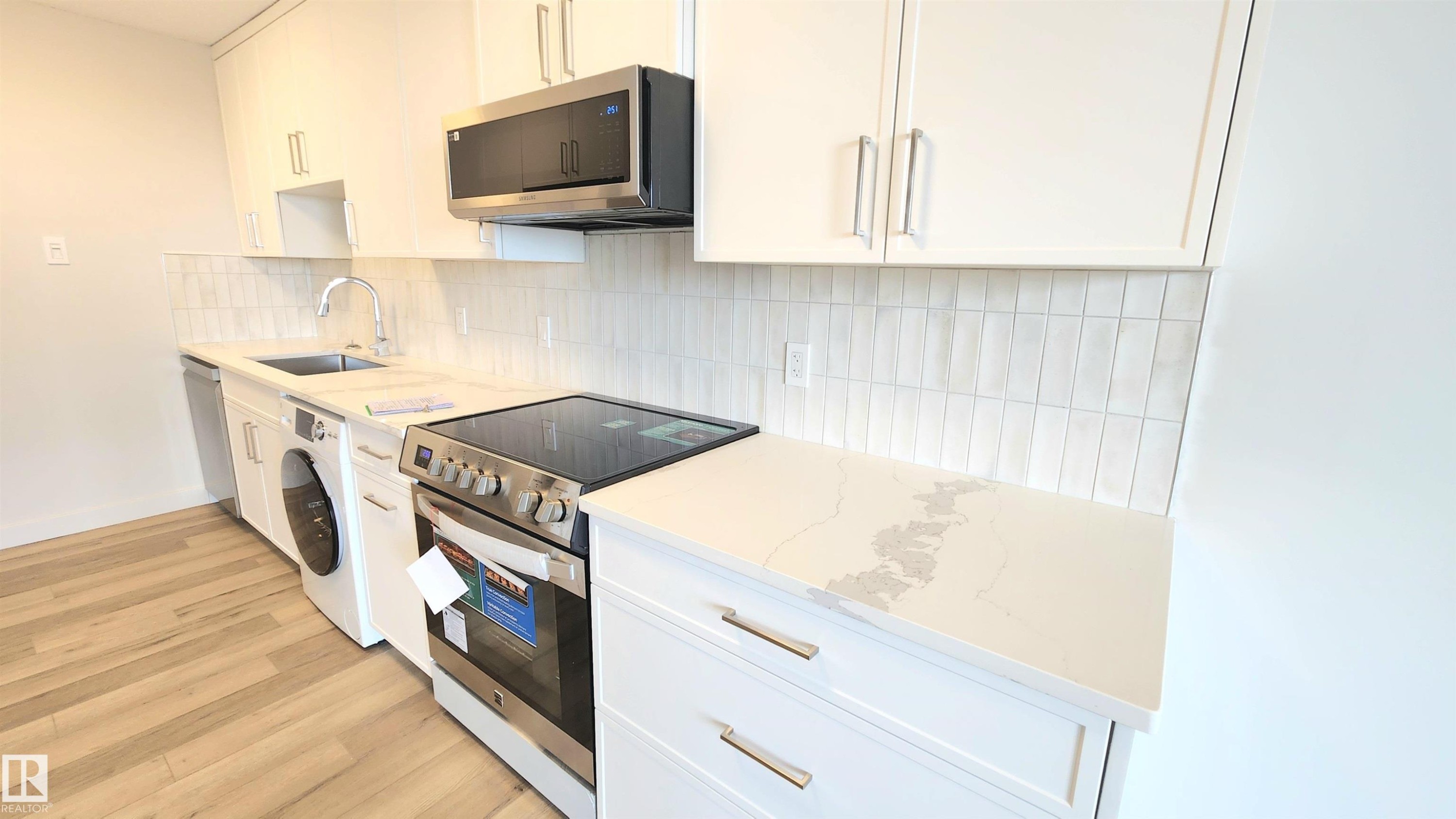 Modern kitchen featuring white cabinetry, light-toned countertops with subtle veining, stainless steel appliances, and a stacked subway tile backsplash - 603 9028 Jasper Avenue, Edmonton, AB - Indoor Photo Showing Kitchen With Upgraded Kitchen