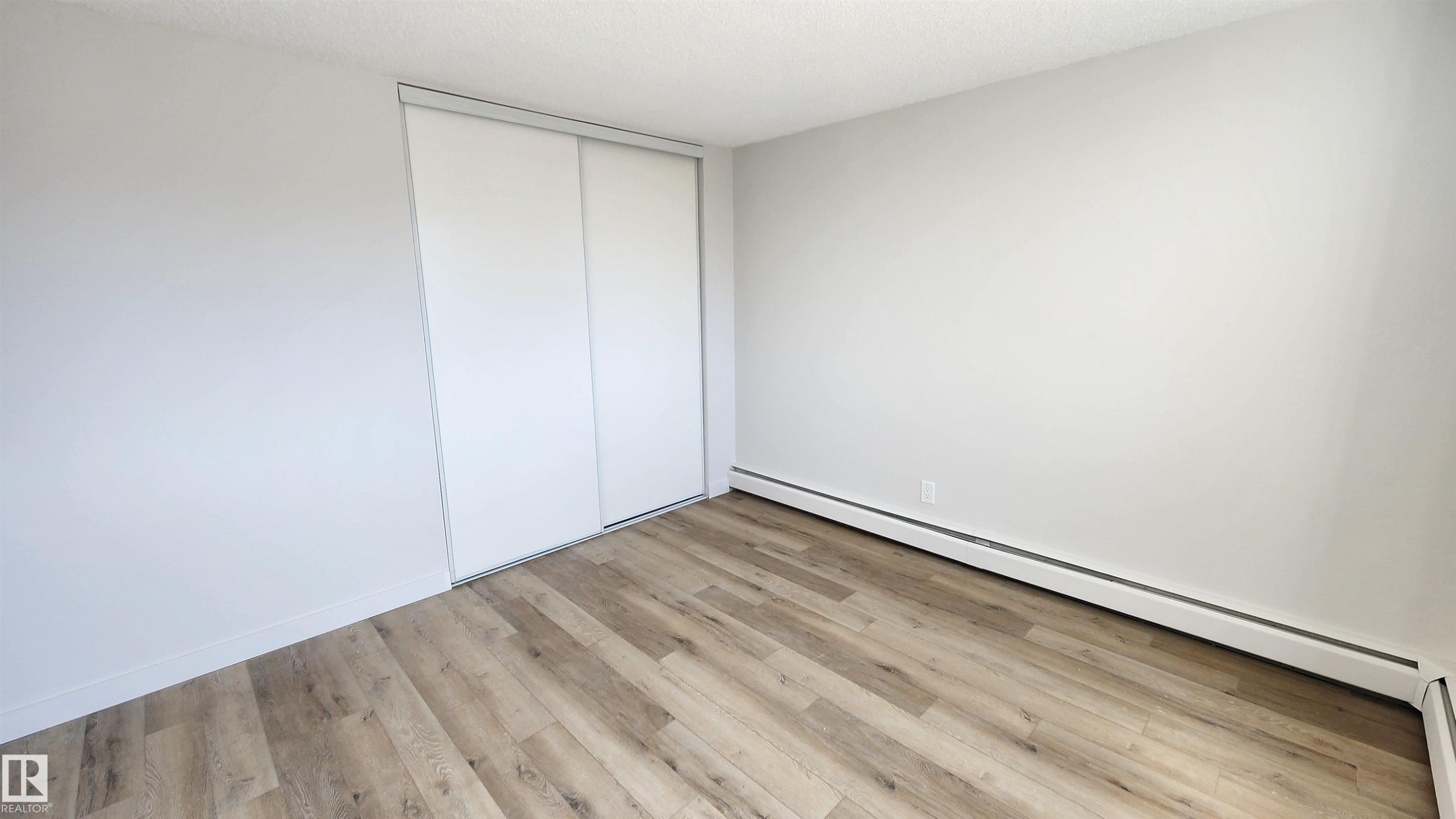 Room featuring wood-finish flooring, white baseboards, and light gray painted walls - 603 9028 Jasper Avenue, Edmonton, AB - Indoor Photo Showing Other Room