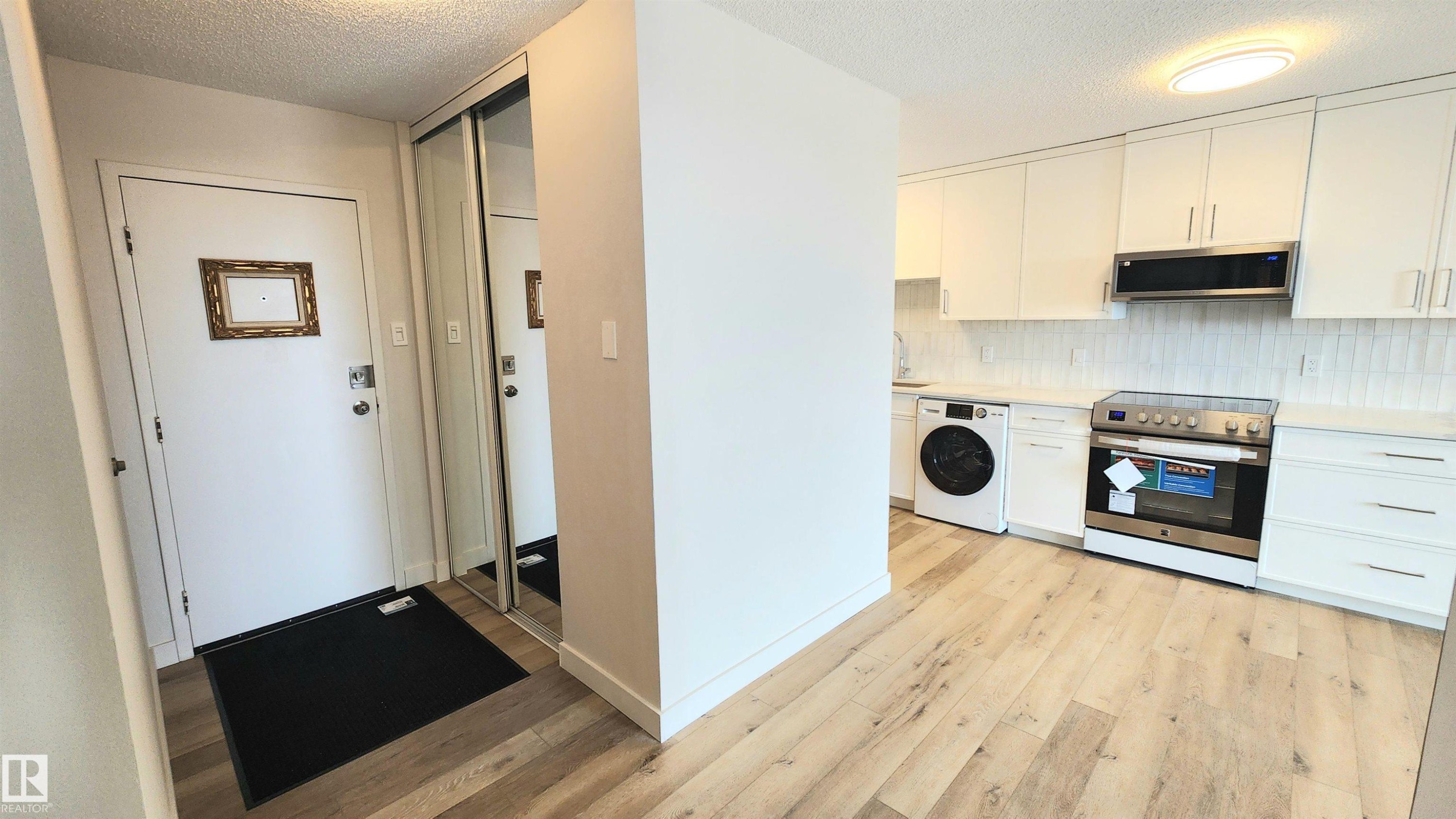 Modern kitchen featuring light wood-finish flooring, white cabinetry, and stainless steel appliances - 603 9028 Jasper Avenue, Edmonton, AB - Indoor