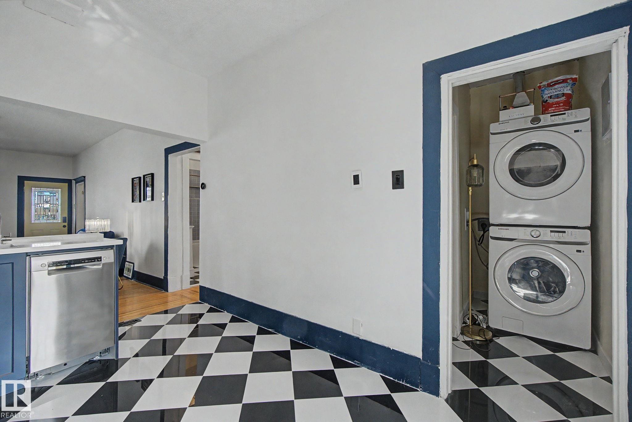 Black and white checkered flooring highlighting a built-in stainless steel dishwasher and a stacked washer and dryer unit - 11512 122 St, Edmonton, AB - Indoor Photo Showing Laundry Room