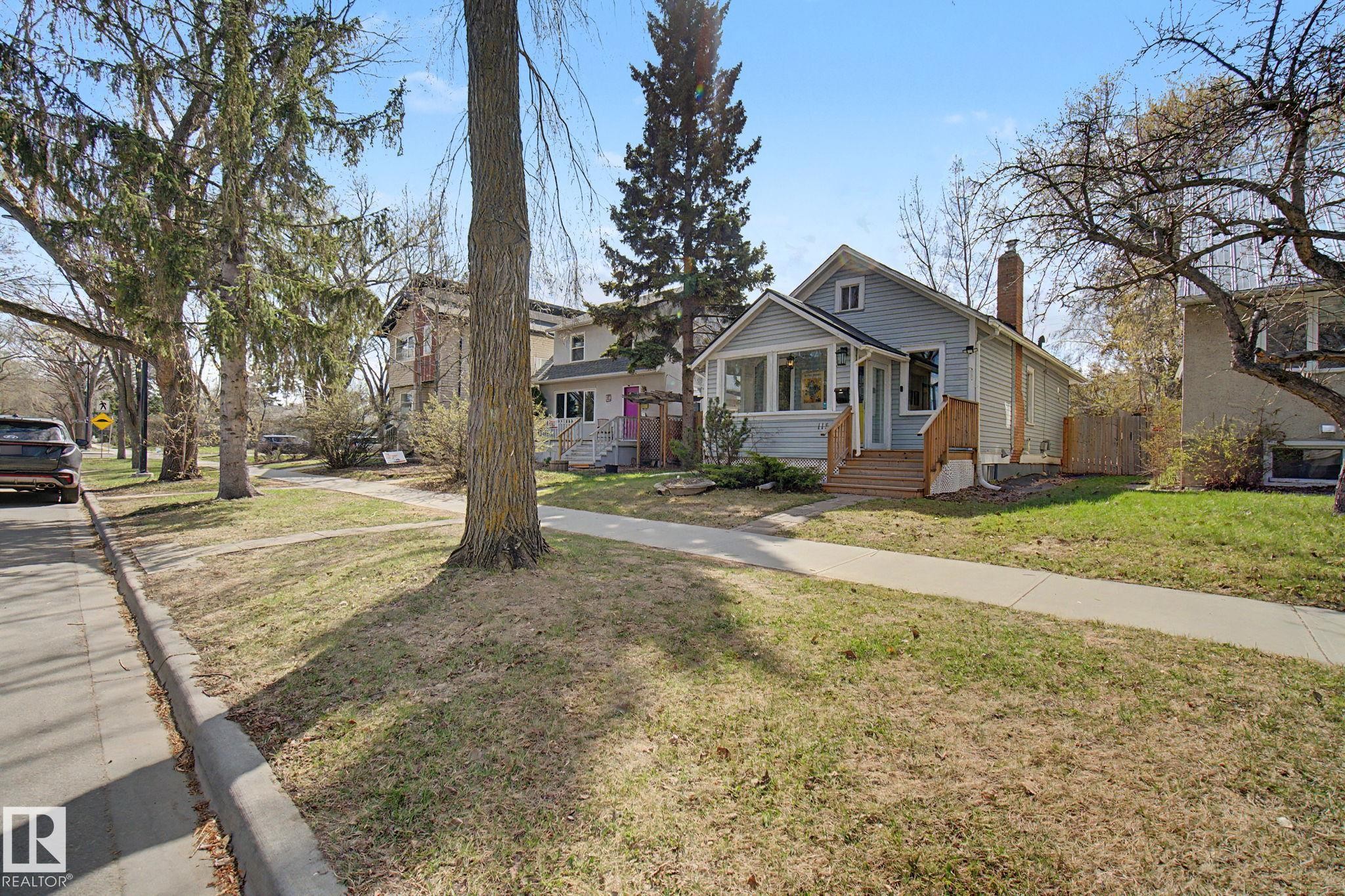 Light blue siding exterior with a contrasting brick chimney and a covered front porch featuring multiple windows - 11512 122 St, Edmonton, AB - Outdoor With Facade