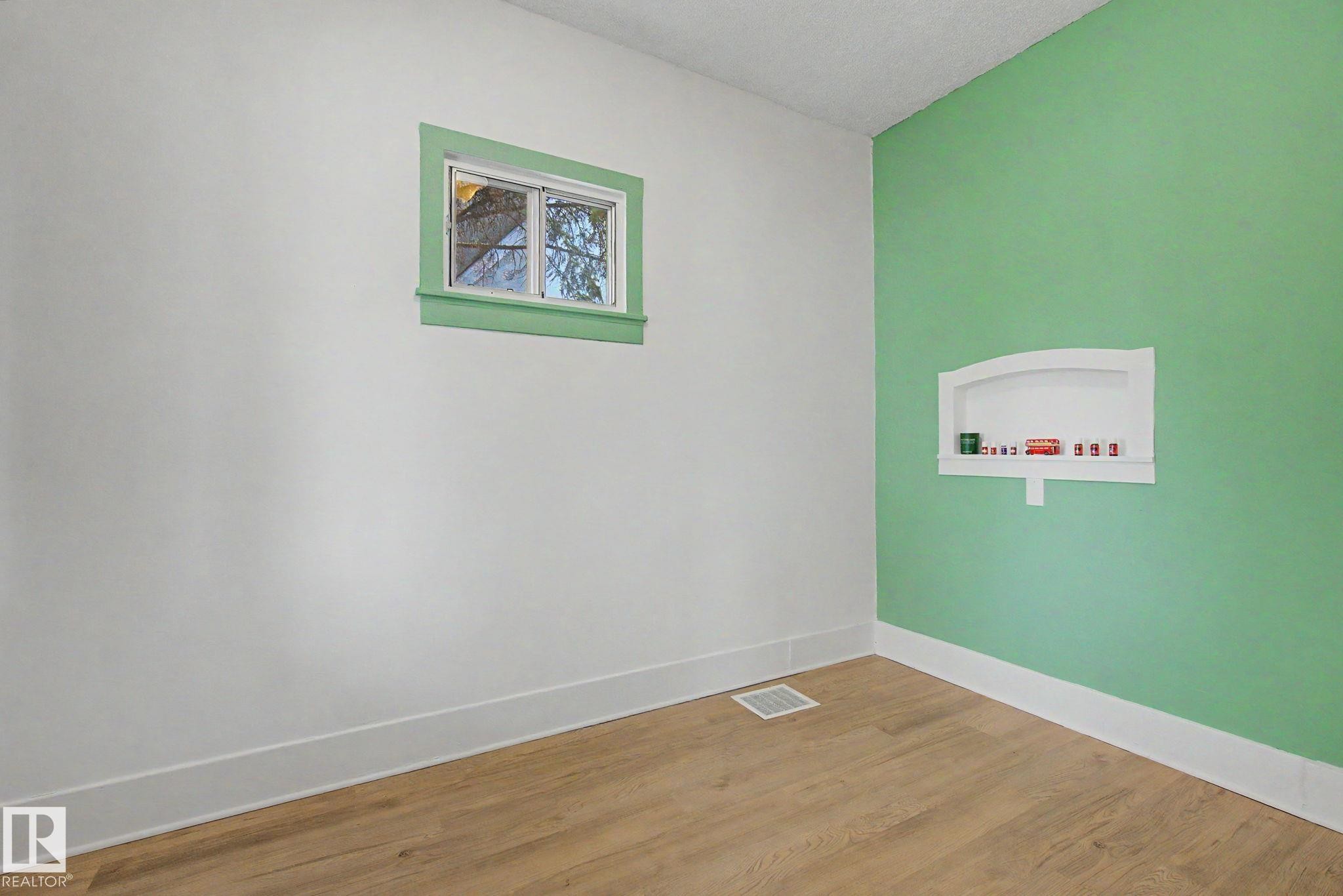 Room with wood-finish flooring, white baseboards, and a window with green trim - 11512 122 St, Edmonton, AB - Indoor Photo Showing Other Room