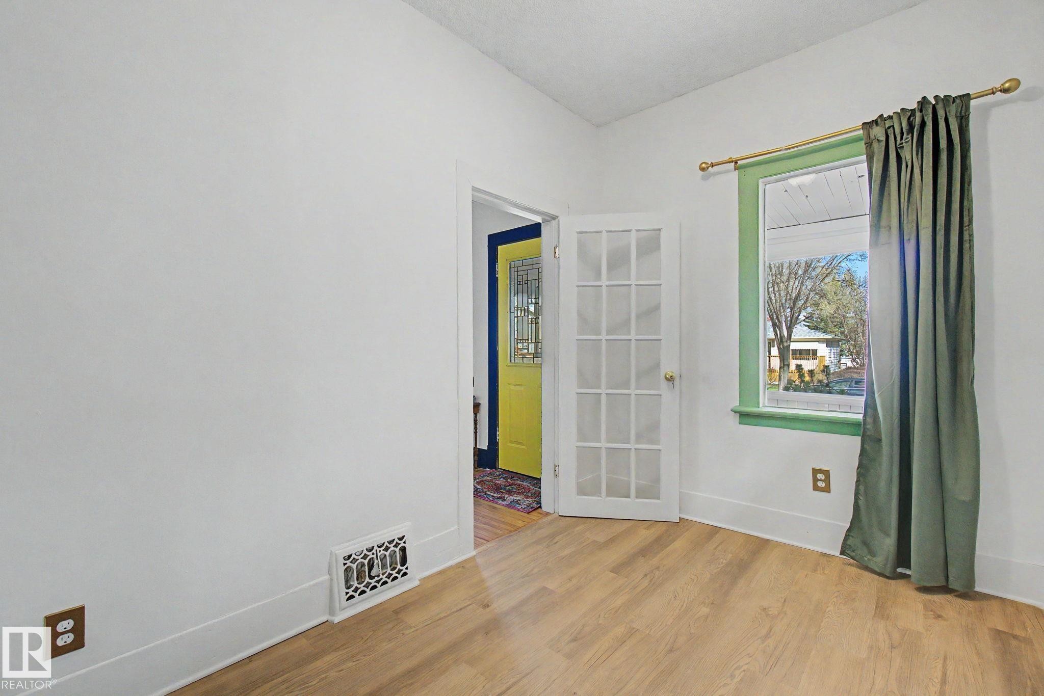 Room featuring wood-finish flooring, white walls, and a window with green trim - 11512 122 St, Edmonton, AB - Indoor Photo Showing Other Room