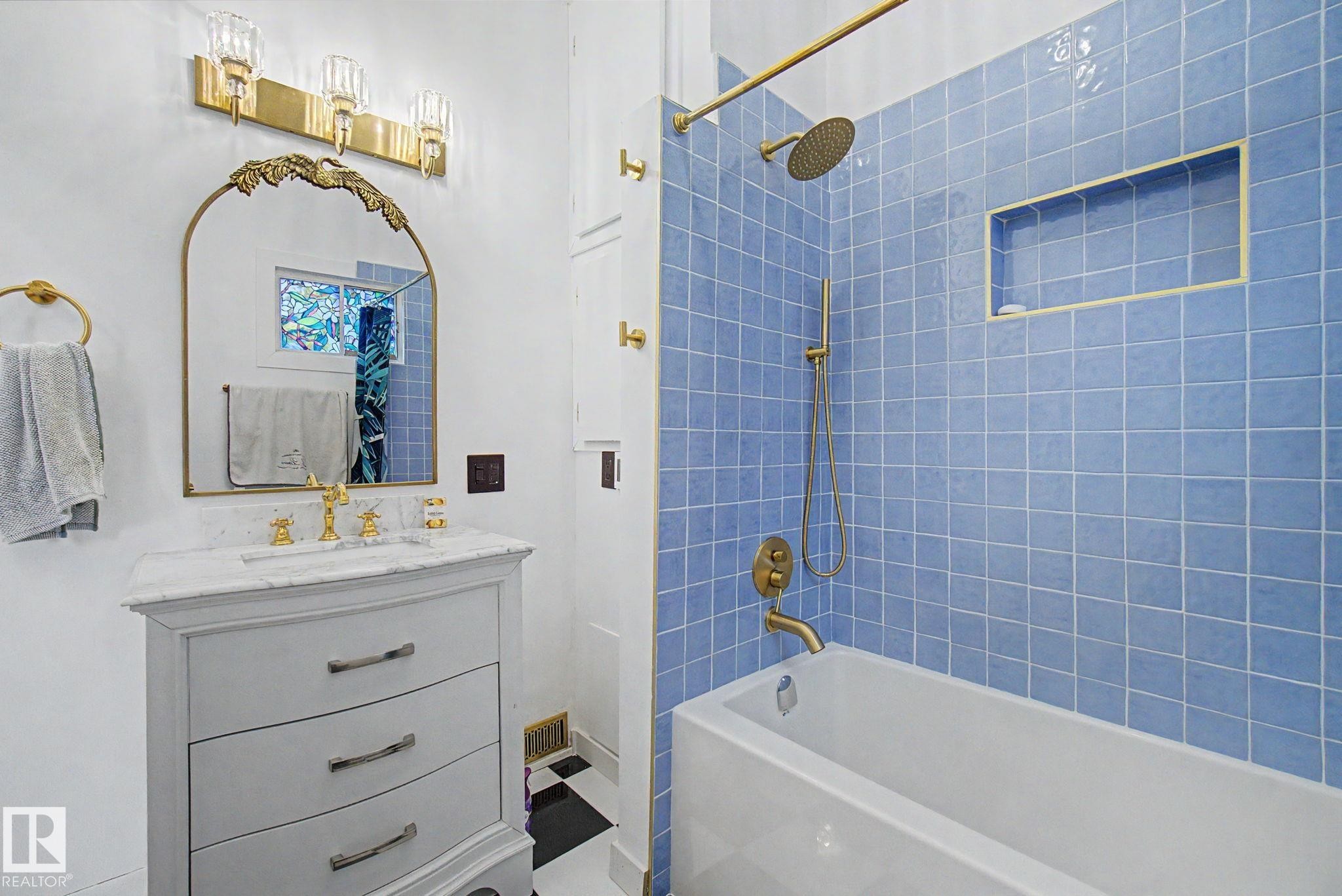 Bathroom featuring a vanity with a white stone countertop, a gold-framed mirror, and a gold-toned light fixture - 11512 122 St, Edmonton, AB - Indoor Photo Showing Bathroom