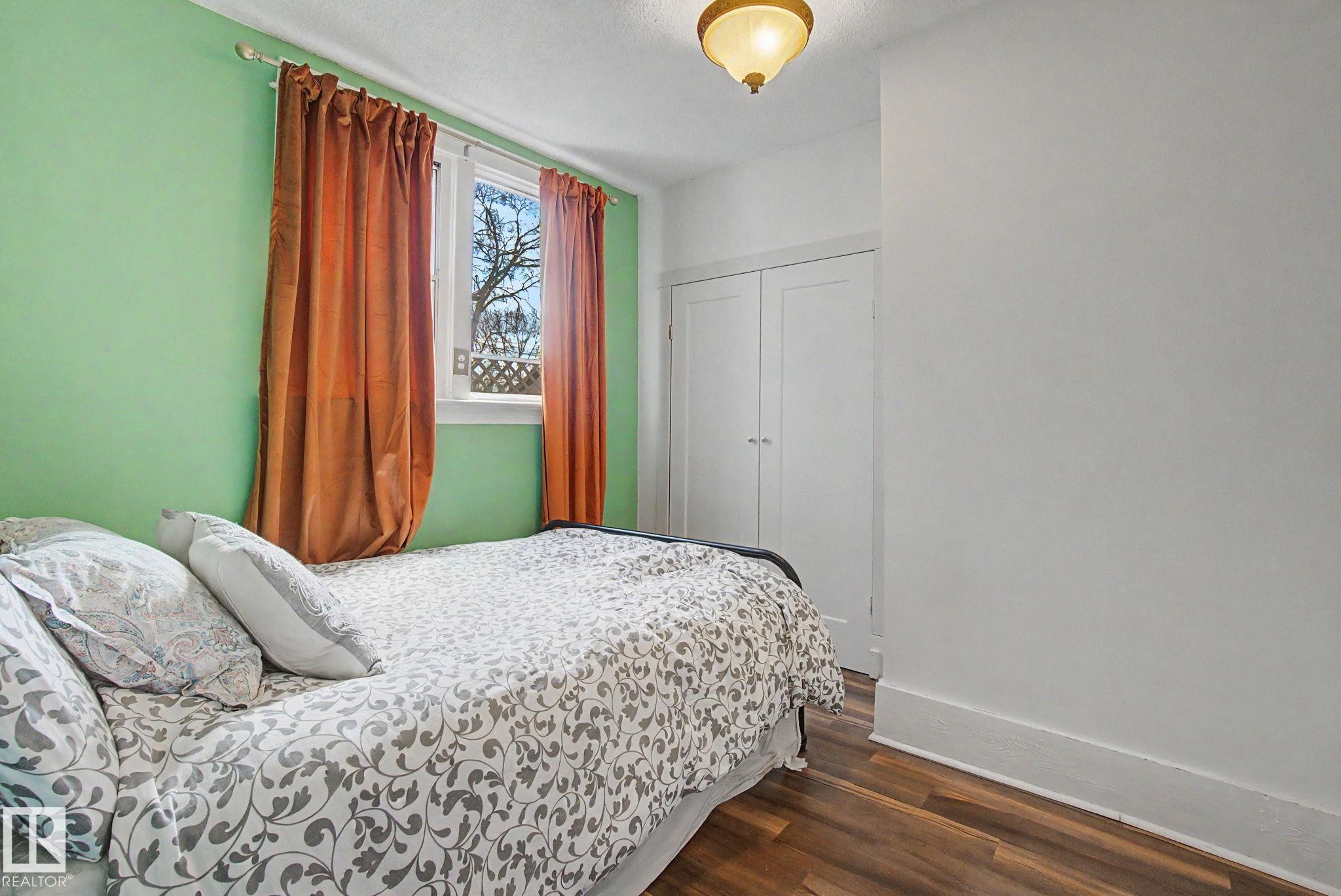 Room featuring wood-finish flooring, a window with natural light, and a built-in closet with double doors - 11512 122 St, Edmonton, AB - Indoor Photo Showing Bedroom