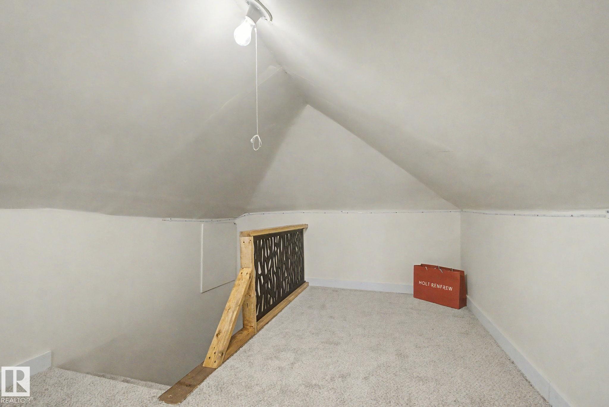 Carpeted loft space with angled ceilings, light-toned walls, and a wood-framed railing with a decorative metal insert - 11512 122 St, Edmonton, AB - Indoor Photo Showing Other Room