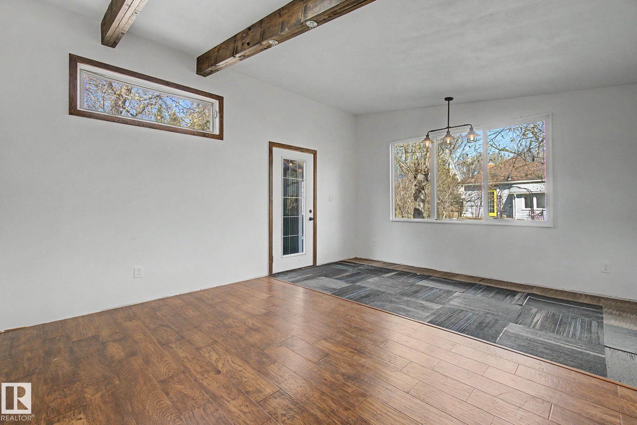 Spacious room featuring exposed wood ceiling beams, wood-finish flooring, and a large multi-pane window - 11512 122 St, Edmonton, AB - Indoor Photo Showing Other Room