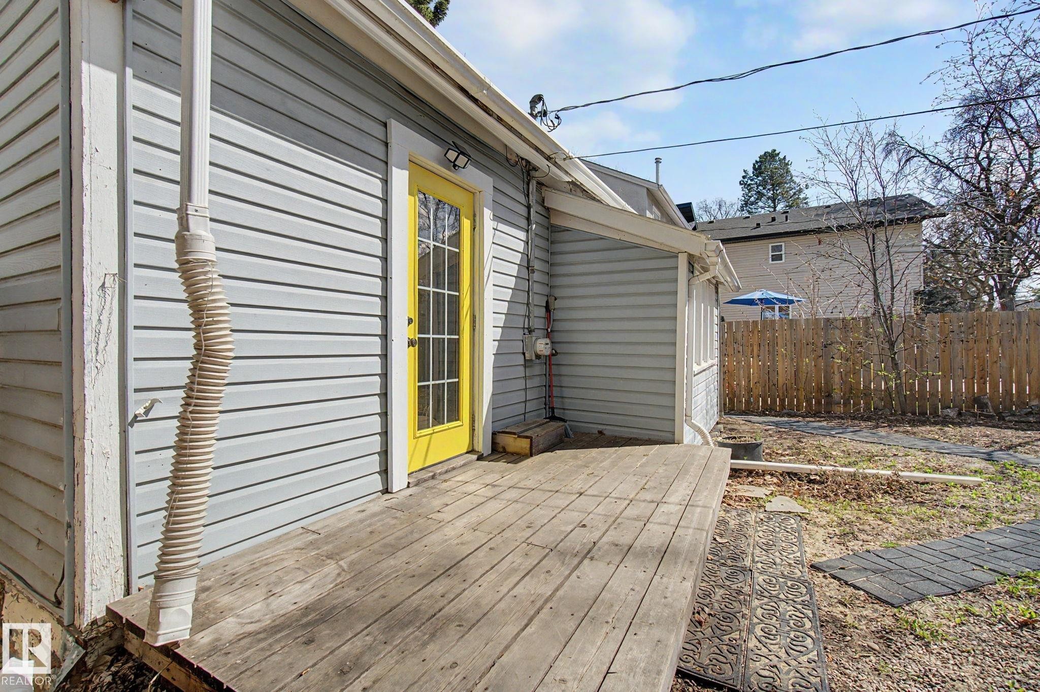Rear exterior featuring light grey siding with white trim, a yellow paneled door, and a wooden deck - 11512 122 St, Edmonton, AB - Outdoor With Exterior